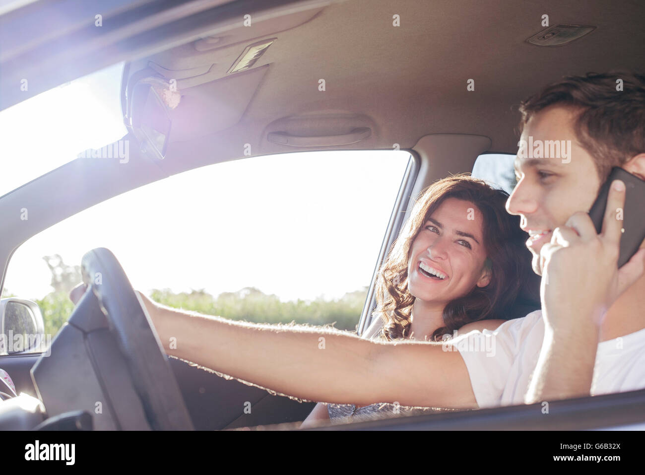 Couple riding in car together while driver chats on cell phone without hands-free device Stock Photo