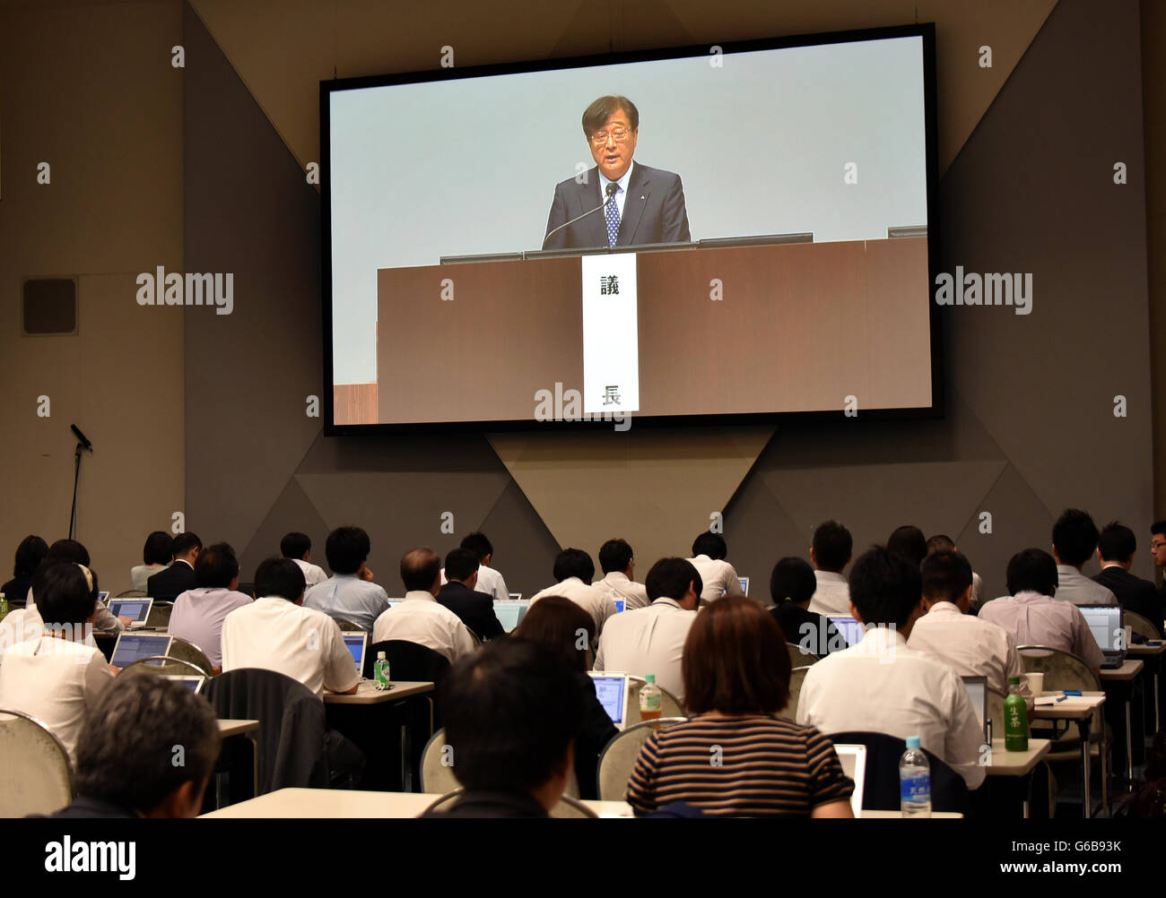 Makuhari, Japan. 24th June, 2016. Reporters take notes as Chairman Osamu Mashiko, on the monitor, of the trouble-stricken Mitsubishi Motors addresses a general stockholders meeting at Makuhari Messe, east of Tokyo, on Friday, June 24, 2016. The Japanese automaker forecast its first loss in eight years after setting aside compensation costs related to manipulating fuel-efficiency ratings and falsifying test data. Net loss in the year ending March 31 will probably be $1.4 billion, the company said in a statement Wednesday. Credit:  Natsuki Sakai/AFLO/Alamy Live News Stock Photo