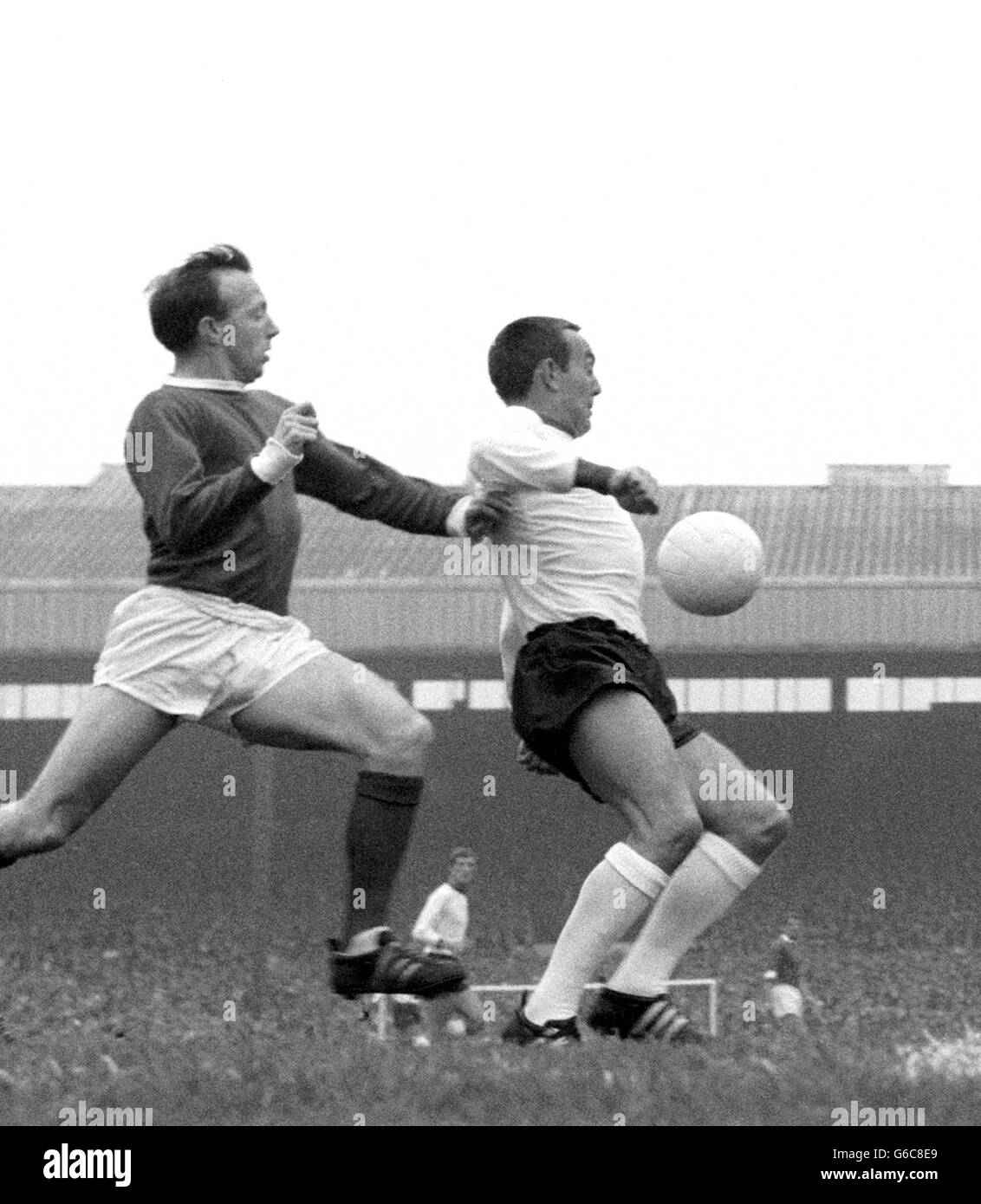 Manchester United wing-half Nobby Stiles (left) appears to be giving a helping shove to Liverpool centre-forward Ian St. John as he races across to clear the ball from danger near the United goalmouth during the match in Manchester. Stock Photo