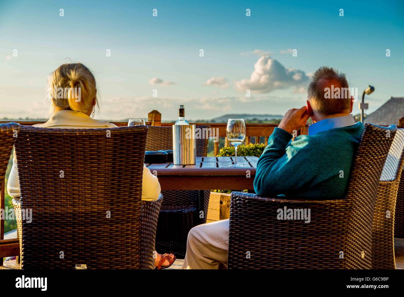 A couple watching the sunset and sun go down while sitting at a table with a bottle of white wine Stock Photo