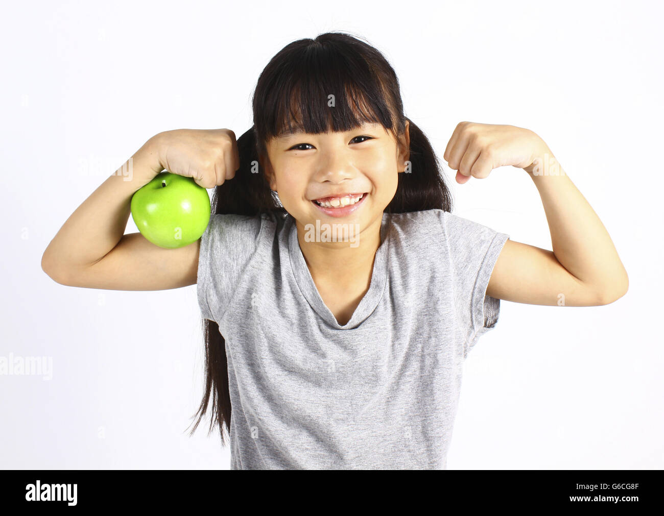 A little girl flexes her muscle while showing off the apple Stock Photo