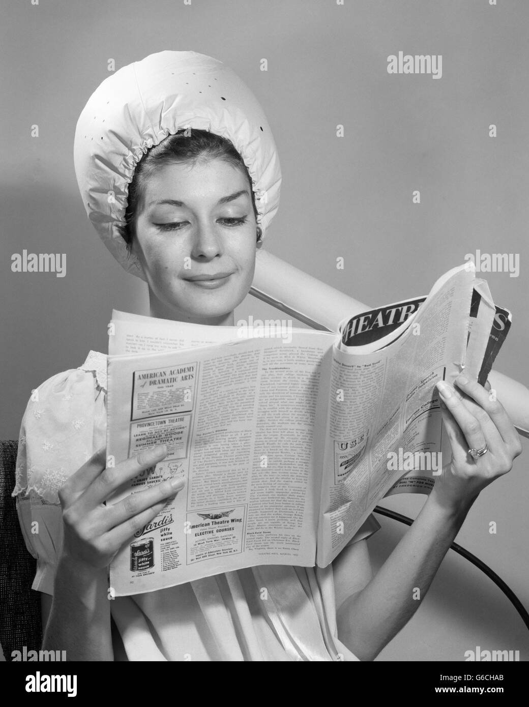 1960s WOMAN SITTING UNDER BONNET STYLE HAIRDRYER HAIR DRYER READING MAGAZINE Stock Photo