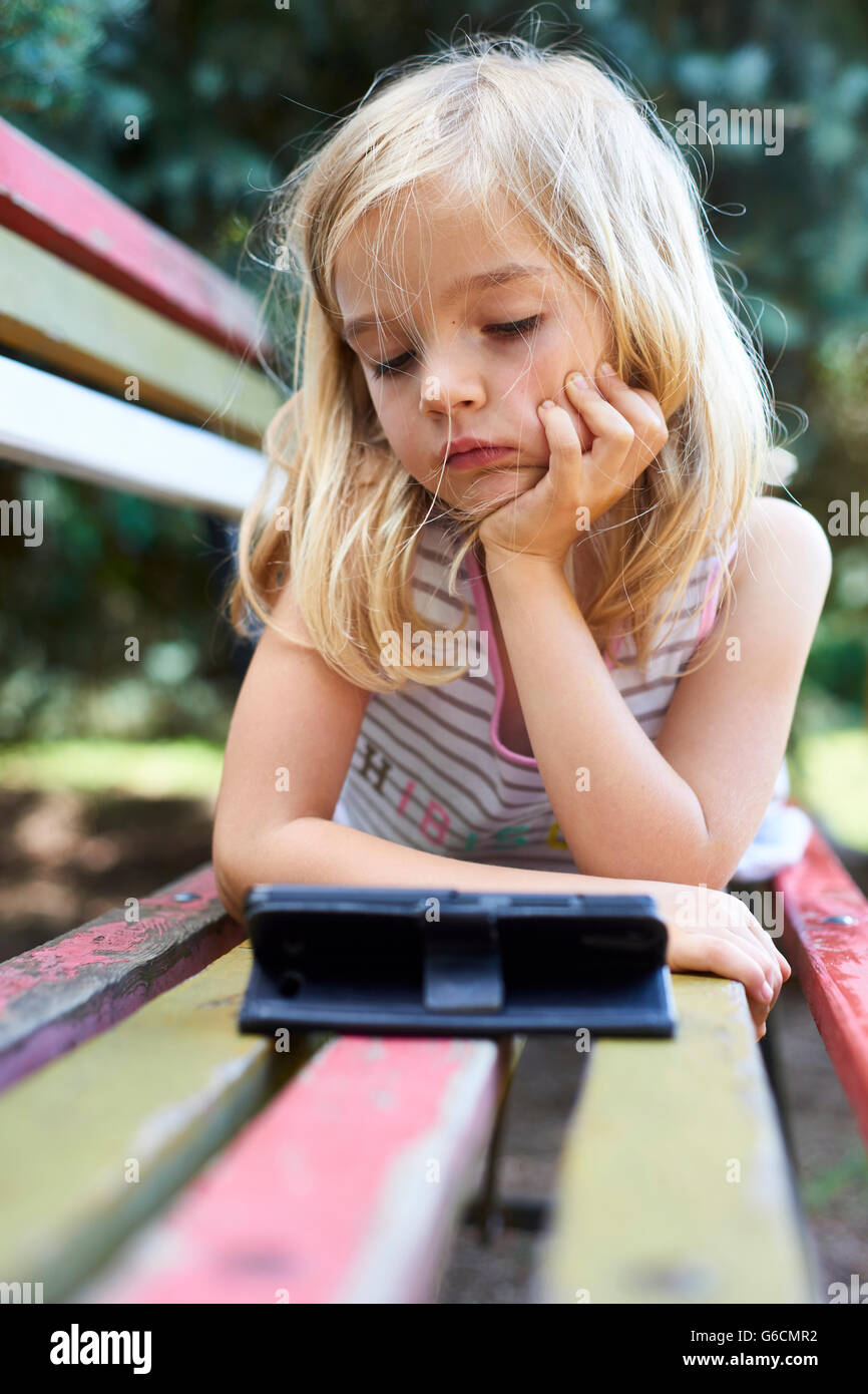 Beautiful Caucasian blond girl sitting on old park bench playing on smart phone Stock Photo
