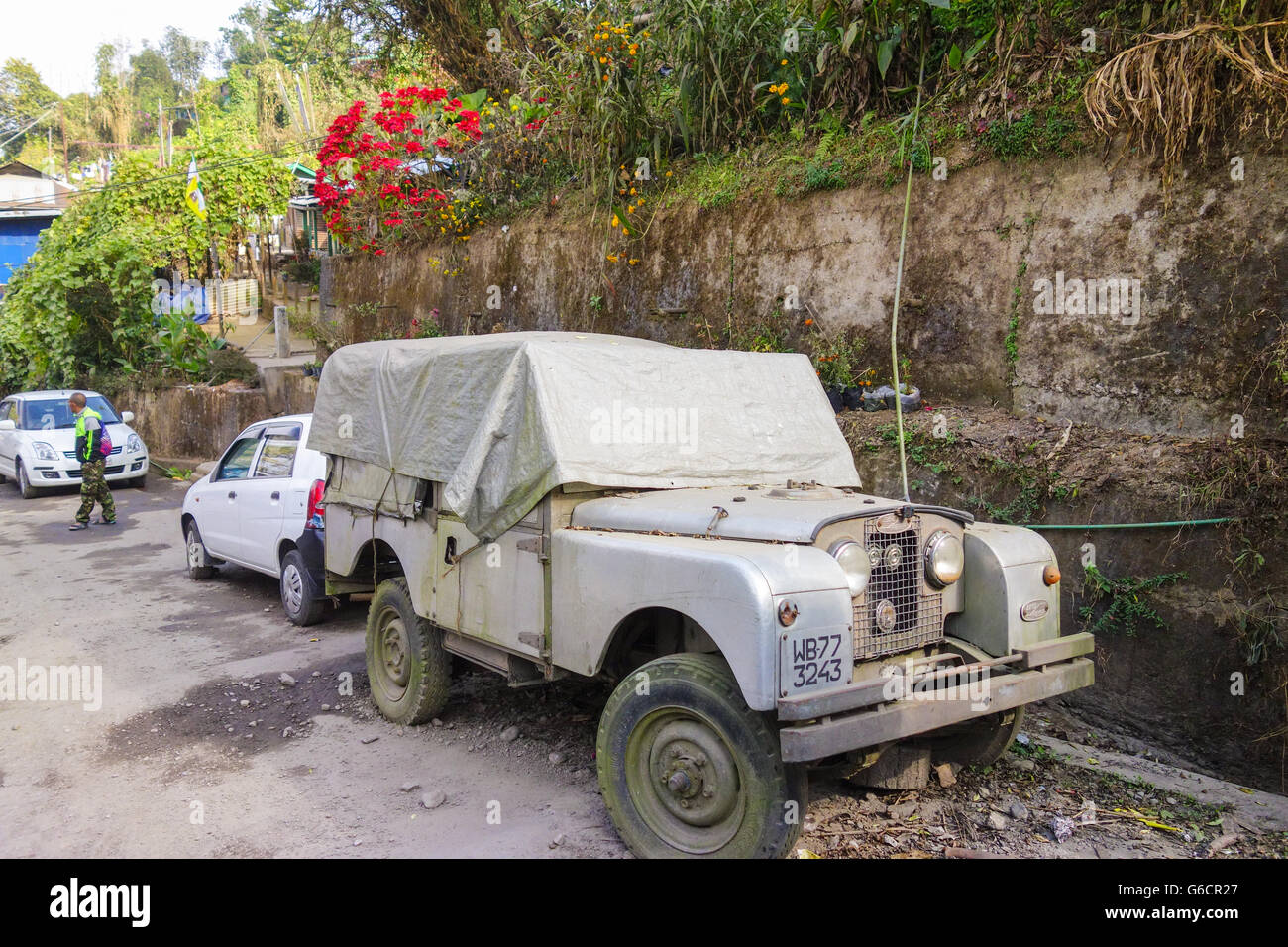 Old unused classic Land Rover Series II car lying partially covered on roadside in Darjeeling Stock Photo