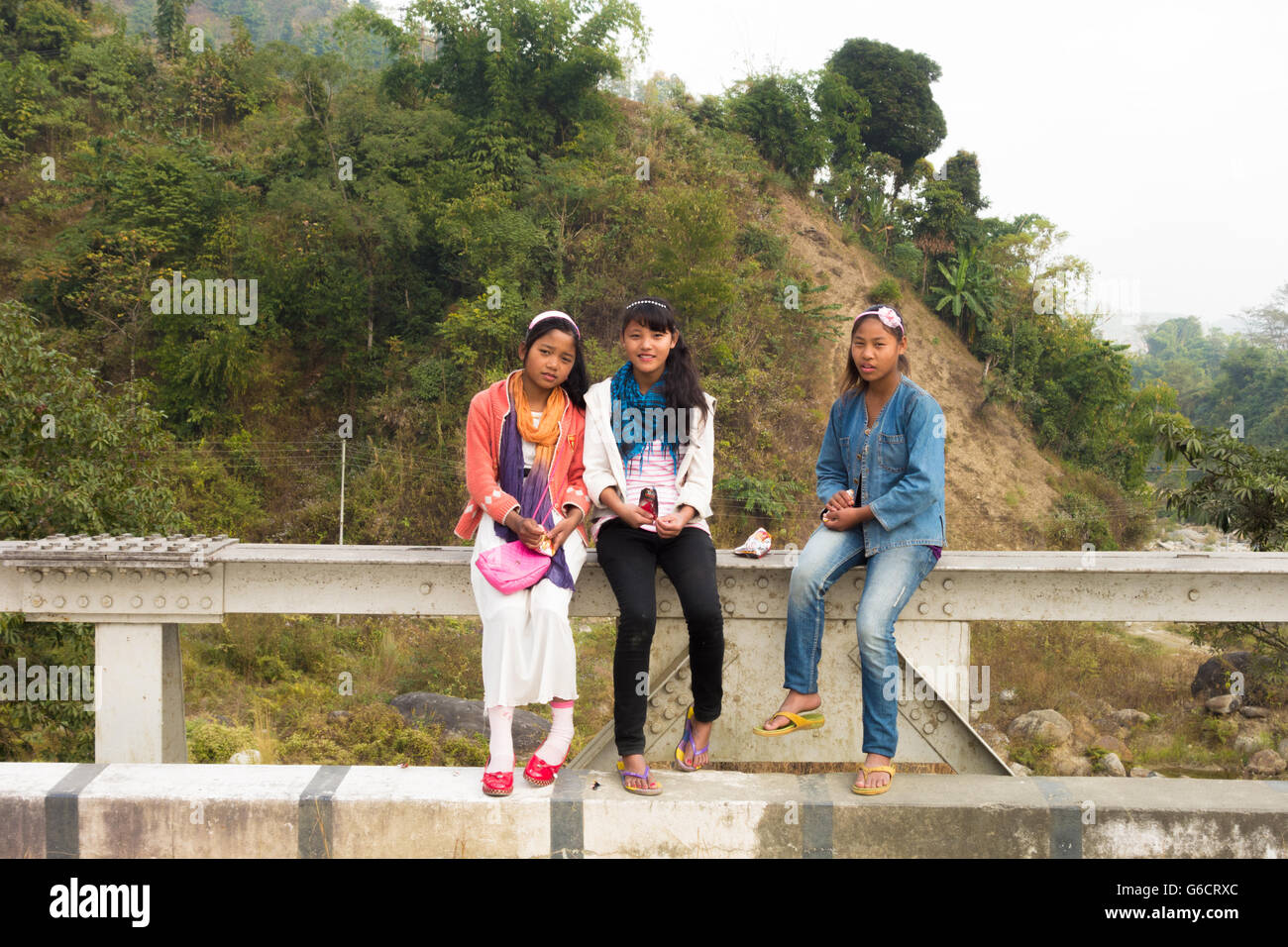 Three young Darjeeling girls sitting on roadside iron railing at Jamuni, Darjeeling, West Bengal, India Stock Photo