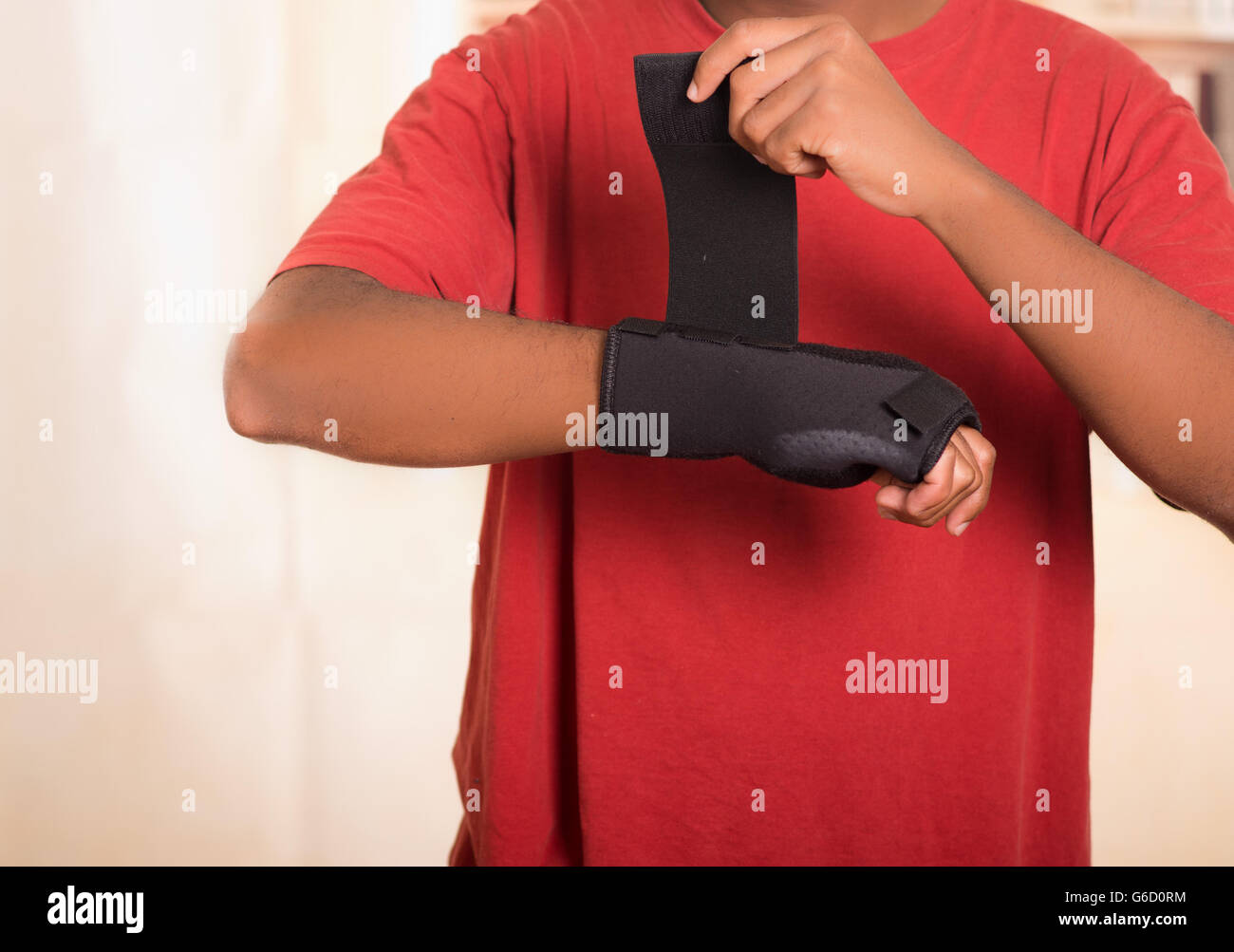 Closeup man in red shirt wearing black wrist brace support on right hand, tightening velcro