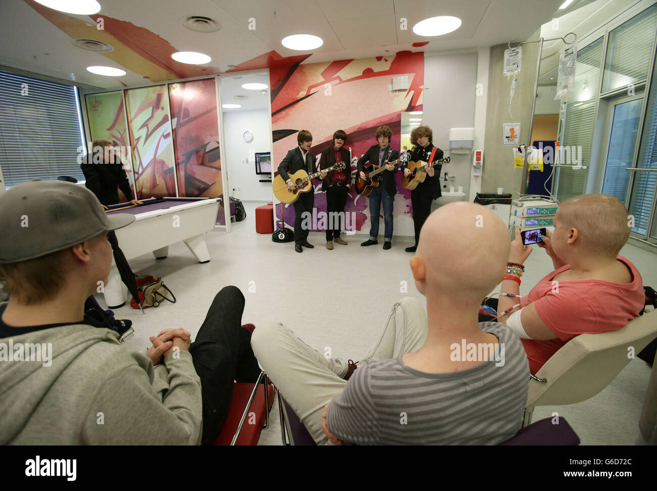 Roger Daltrey CBE (background left), Patron of Teenage Cancer Trust, and current patients watching as band The Strypes (left to right) Josh McClorey, Ross Farrelly, Pete O'Hanlon and Evan Walsh play during their visit and gig at a specialist Teenage Cancer Trust unit at University College Macmillan Cancer Centre, central London. Stock Photo