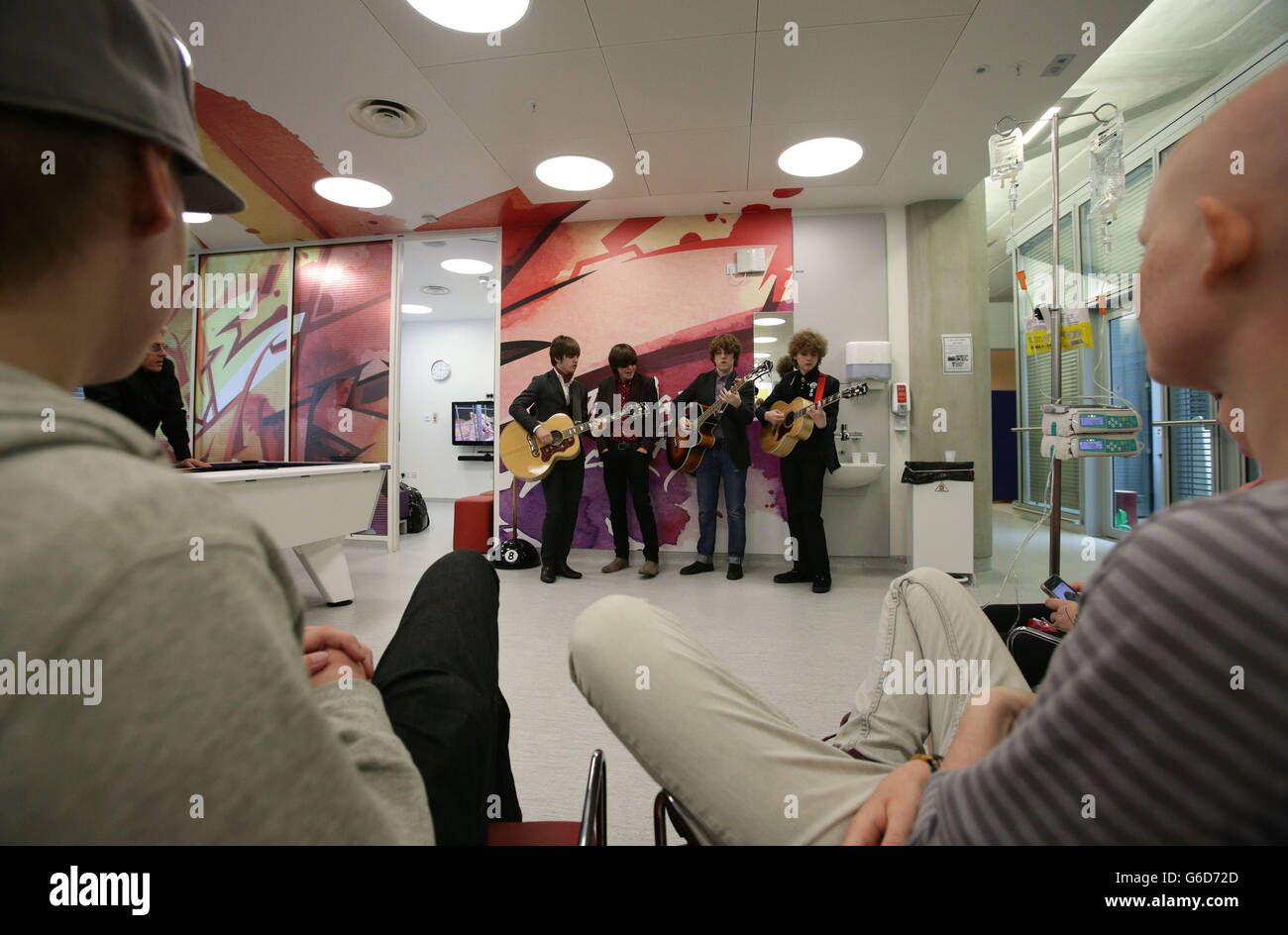 Roger Daltrey CBE (background left), Patron of Teenage Cancer Trust, and current patients watching as band The Strypes (left to right) Josh McClorey, Ross Farrelly, Pete O'Hanlon and Evan Walsh play during their visit and gig at a specialist Teenage Cancer Trust unit at University College Macmillan Cancer Centre, central London. Stock Photo