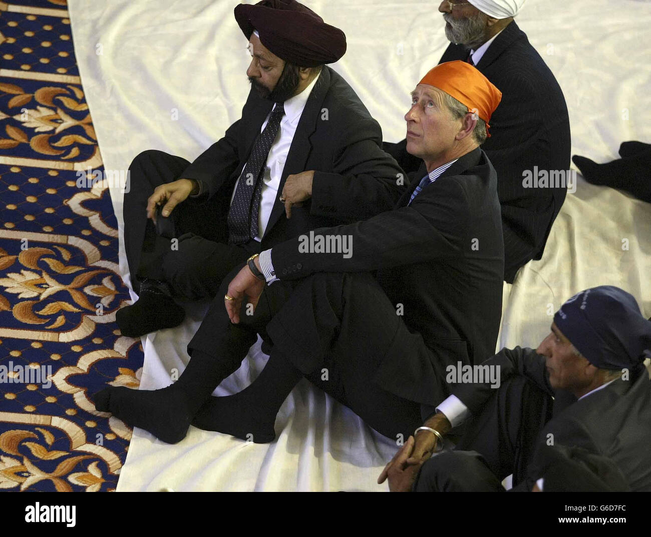 The Prince of Wales, wearing a bright orange Ramal headscarf at the Sri Guru Singh Sabha Gurdwara Sikh Temple, in Southall. * The Prince also removed his shoes in respect for the Sikh religion before being led to the service where he sat cross-legged on a cushion. A welcome hymn was read for the Prince in the prayer hall. He was then presented with a Siropa at the altar - a ceremonial sword, a robe of honour, a shawl for the Queen, and a commemorative book. Stock Photo