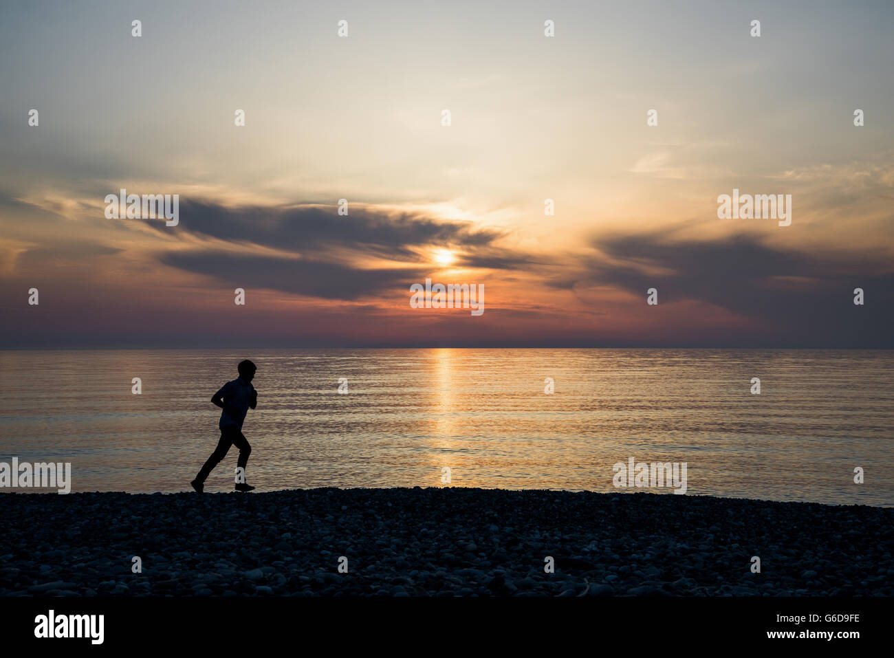 Backlight of a man running on the beach at sunset with the horizon in ...
