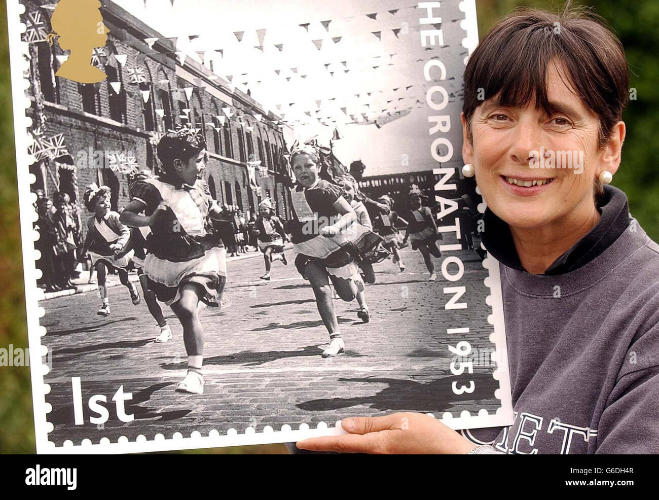 Lorraine Cross, 56, holds a poster sized copy of a new Royal Mail stamp, which is one of ten on sale. The stamp shows her winning a running race in Morpeth Street, Bethnal Green, London, during the celebrations for the Coronation of Queen Elizabeth II in 1953. Stock Photo