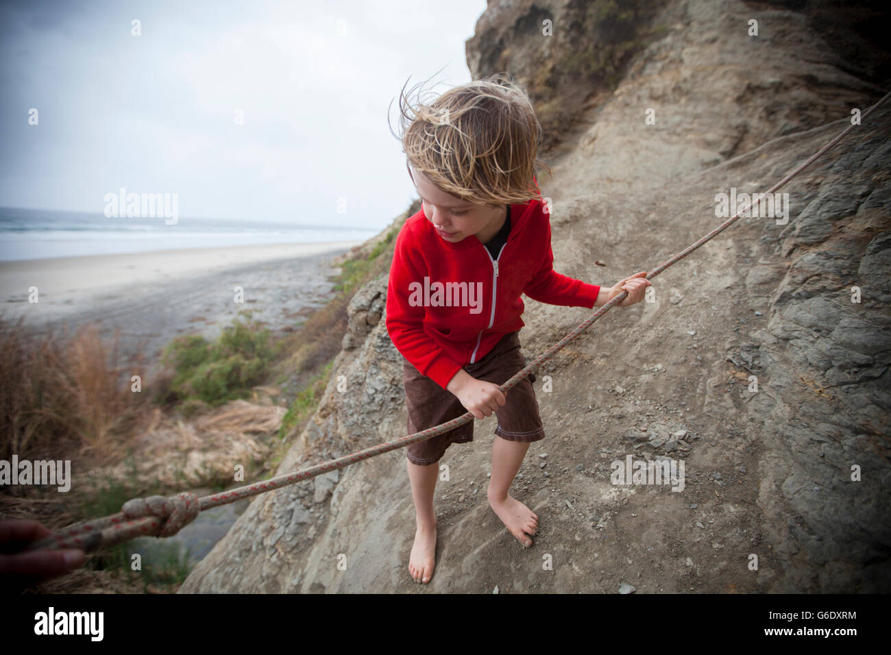 Boy age 5 using the rope to get down the wall to Blacks Beach, La Jolla, California. Stock Photo
