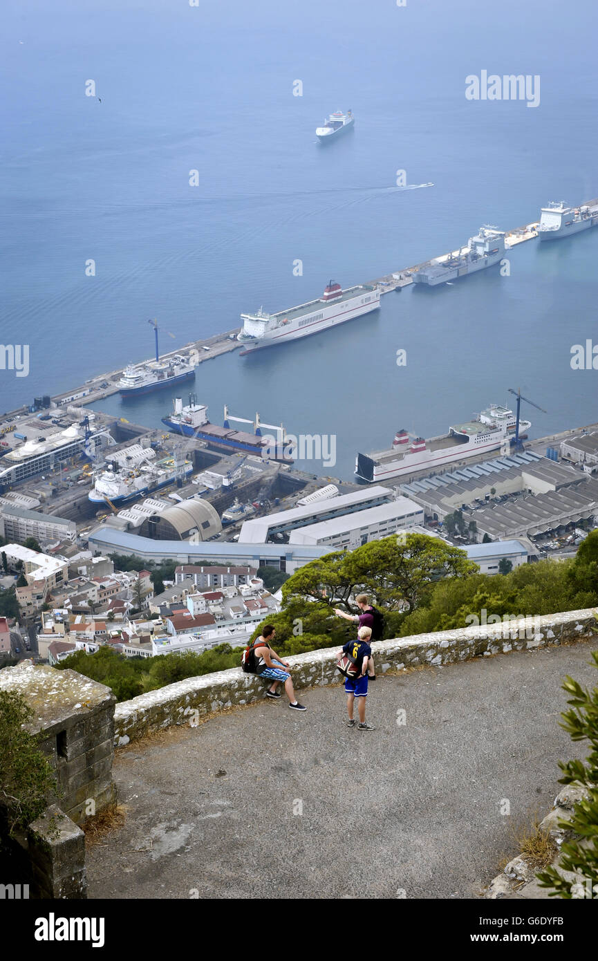 Tourists pause as they climb the Rock of Gibraltar with the harbour and Royal Navy Base at Gibraltar in the background. Stock Photo