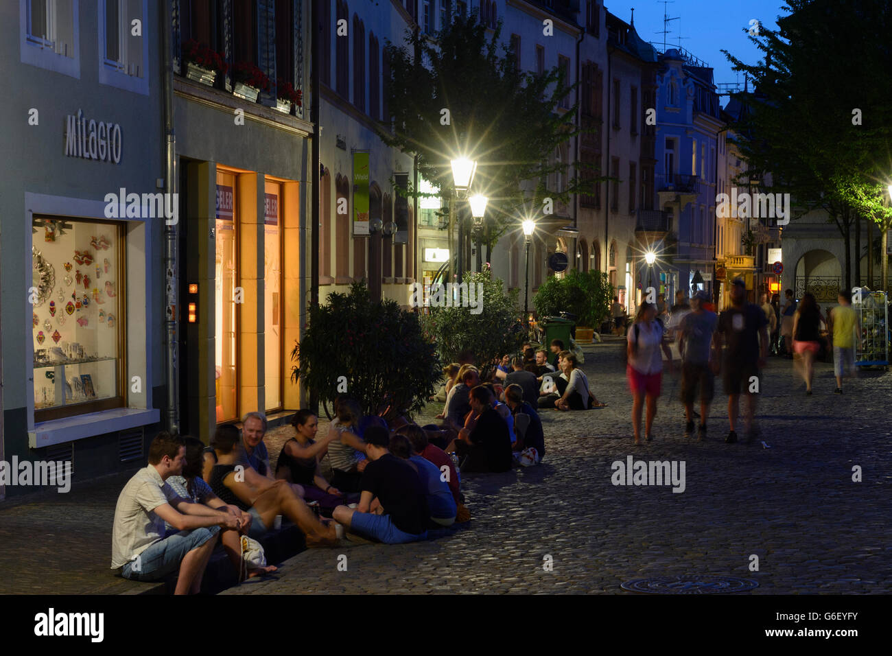 students talking and drinking sitting on a gutter (Bächle) at the square Augustinerplatz, Freiburg im Breisgau, Germany, Baden-W Stock Photo