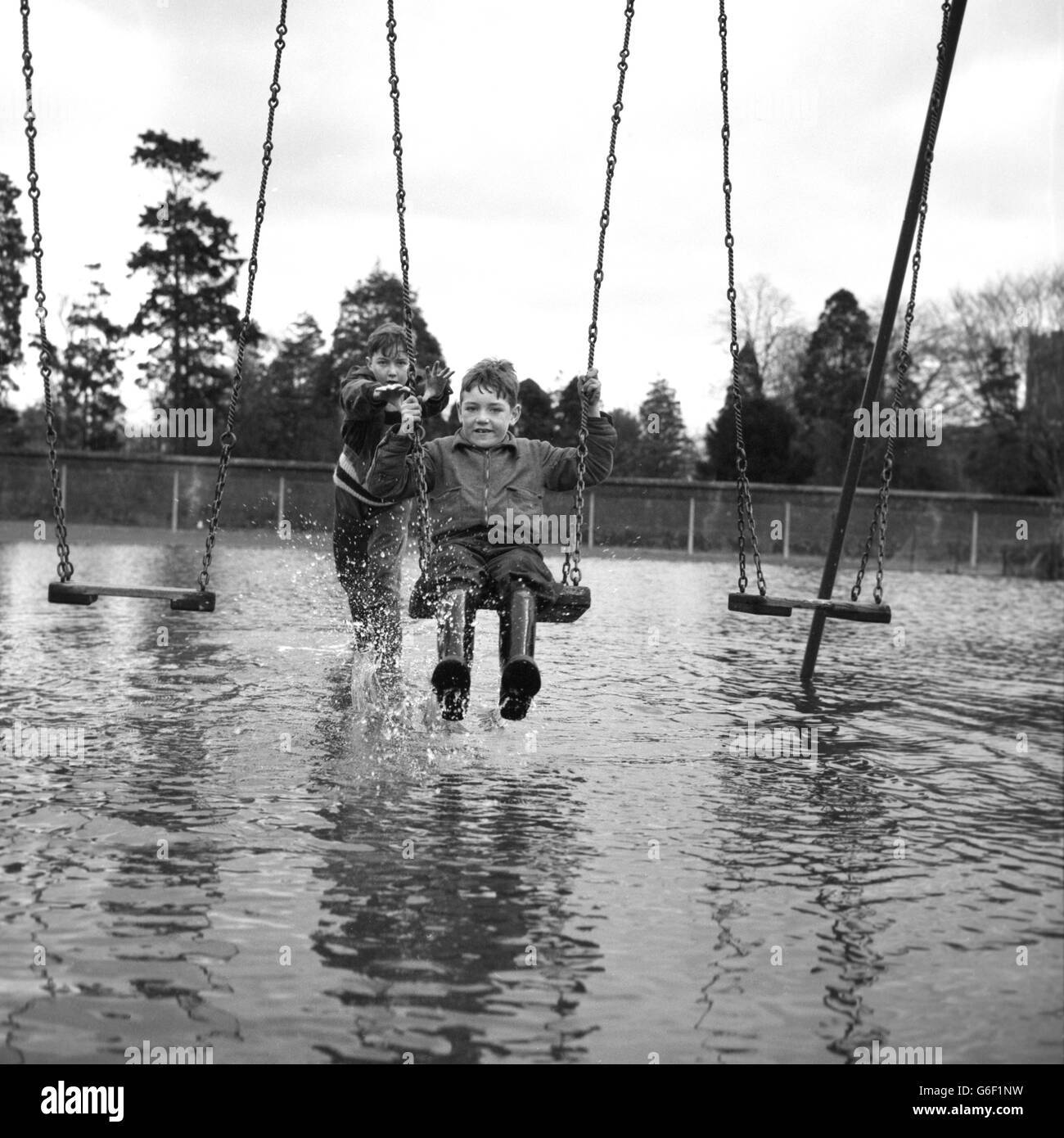 Two boys, of Hythe End, near Staines, Middlesex, get away from the widespread flooding which is causing damage across South England by playing on the swings in the Lammas Recreation Ground in Staines. Stock Photo