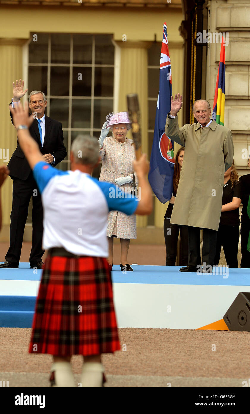 Former athlete Alan Wells waves as he carries the Queen's Baton, watched by the Queen Elizabeth II and Duke of Edinburgh, inside the forecourt of Buckingham Palace in central London, ahead of the start of the sporting event's global relay. Stock Photo