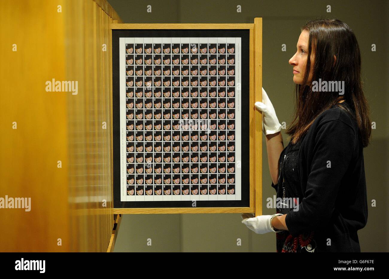 Samantha Howard from The Imperial War Museum North, views stamps bearing pictures of Lance Corporal Thomas Keys, killed in Iraq from Steve McQueen's 'Queen and Country' installation, during a press viewing of the exhibition Catalyst: Contemporary Art and War, which runs from the 12 October 2013 - 23 February 2014, at the IWM North. Stock Photo