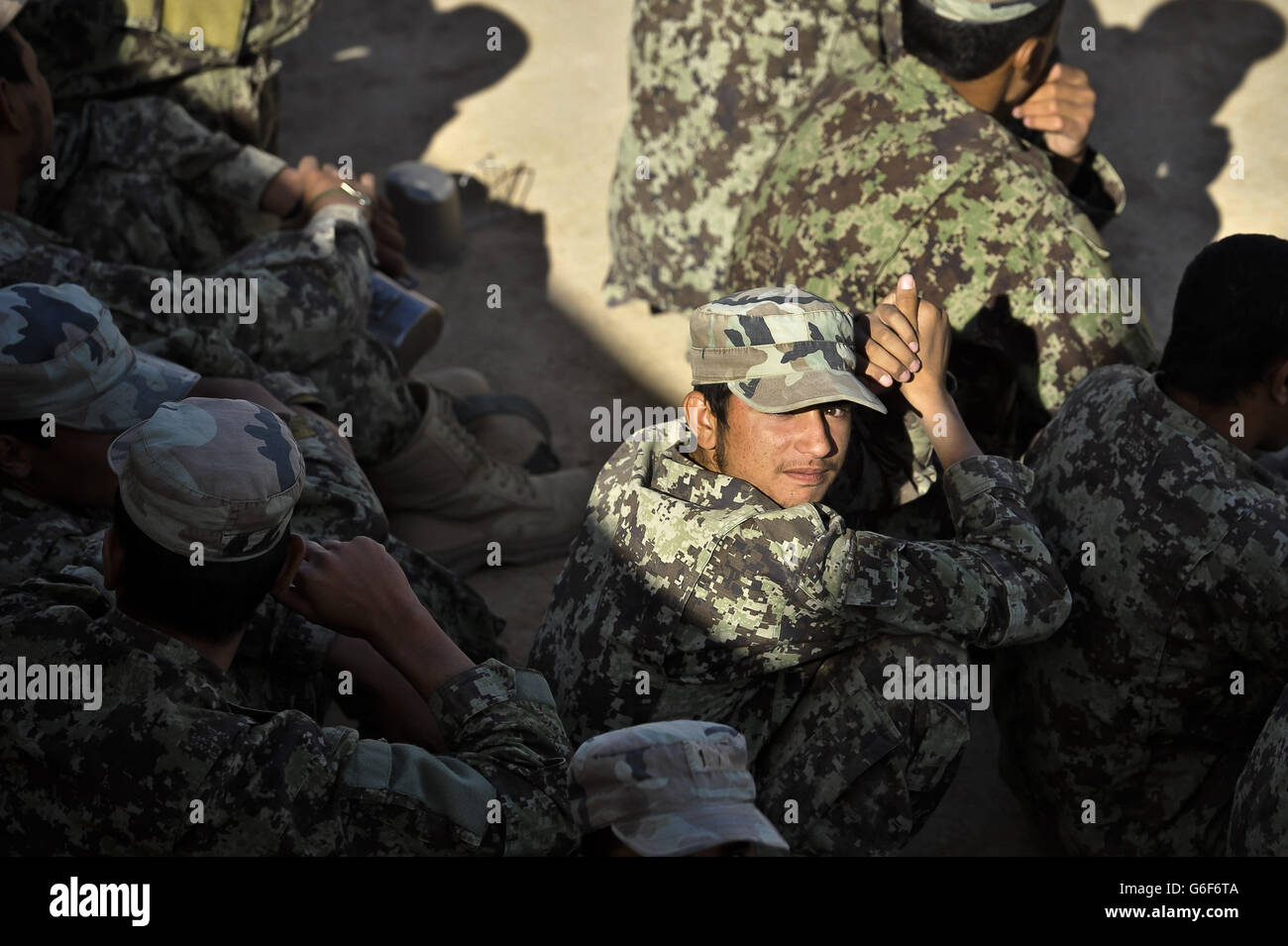 An Afghan National Army (ANA) soldier sits in the shade with his fellow soldiers during a break between training sessions at ANA Camp Shorabak, Helmand Province, Afghanistan. Stock Photo