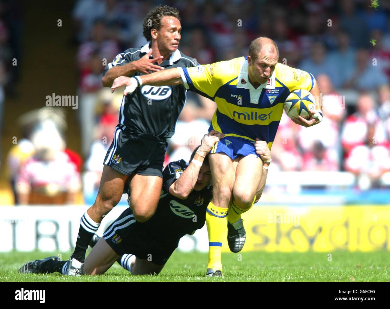 Warrington's Darren Burns is tackled by Wigan's Adrian Lam (L) and Martin Aspinwall, during their Tetlys Super League match at the Wilderspool Stadium in Warrington. Stock Photo