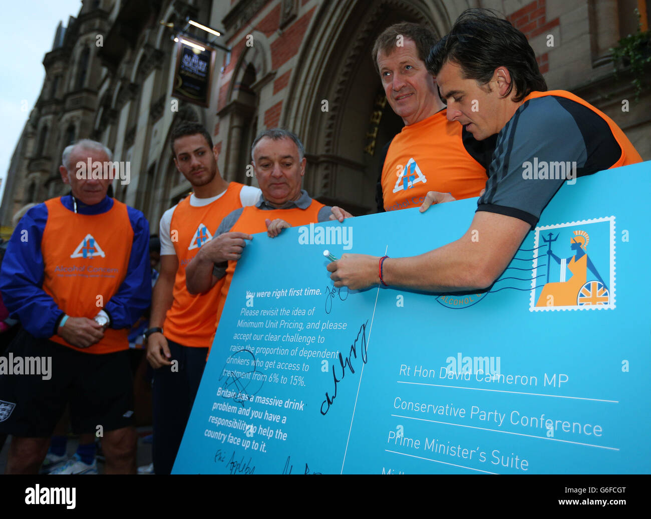 Footballer Joey Barton (right) adds his signature to a postcard, held by Alastair Campbell (second right), which is to be sent to Prime Minister David Cameron at the start of the second day of the Conservative Party Conference at Manchester Central in Manchester. Stock Photo