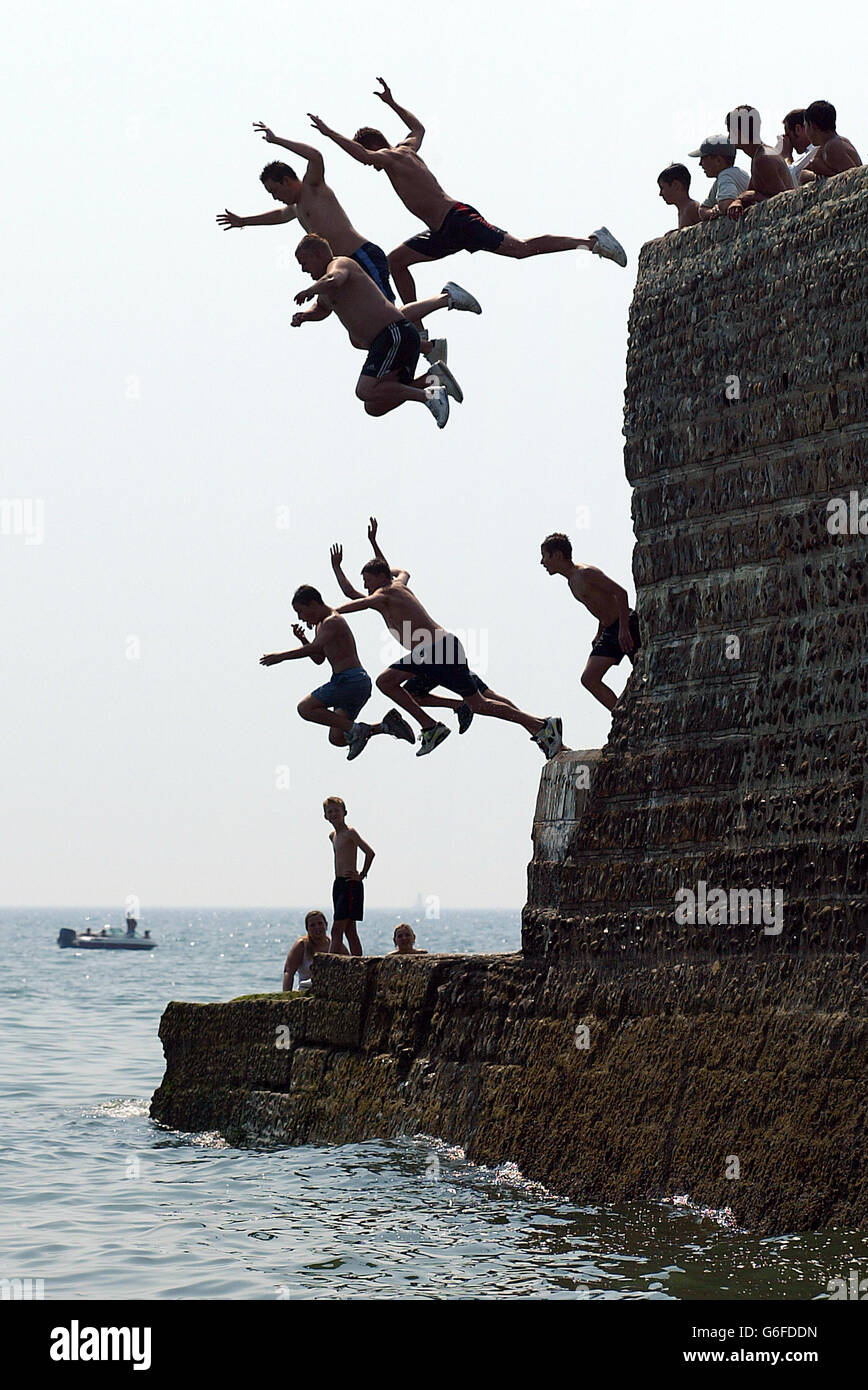 Teenagers leap from the sea wall to cool down in Brighton, West Sussex, as temperatures soared across the country. Stock Photo