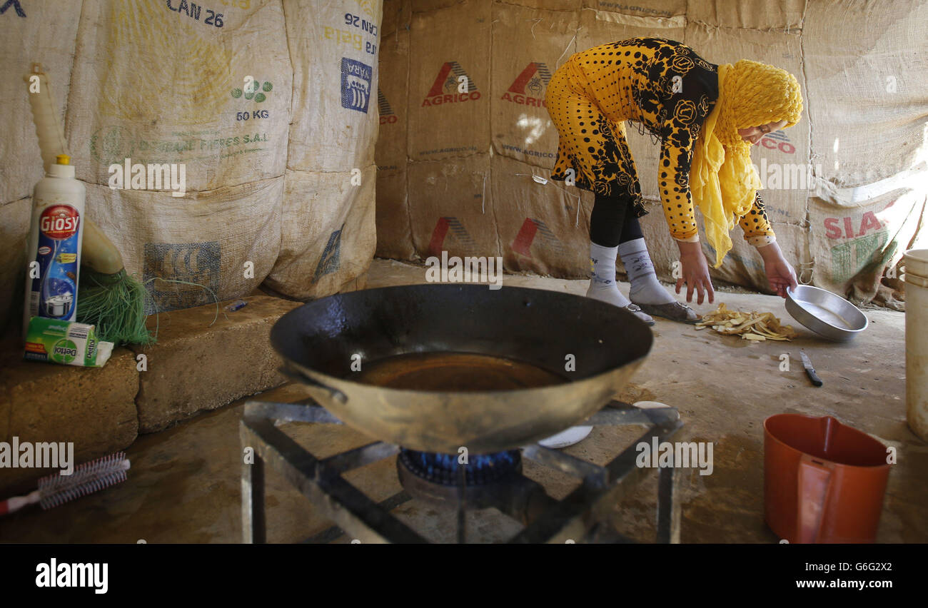 Refugee Kawssar Adawiye, 18, who is pregnant with her second child, prepares food on the floor in the makeshift settlement of Qab Elias in the Bekaa Valley, Lebanon. Stock Photo