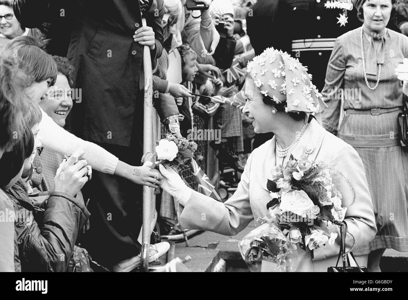 The Queen accepts a floral tribute from a youngster during her walkabout in Coronation Gardens, Dudley, as her Silver Jubilee tour of the West Midlands got under way. Stock Photo