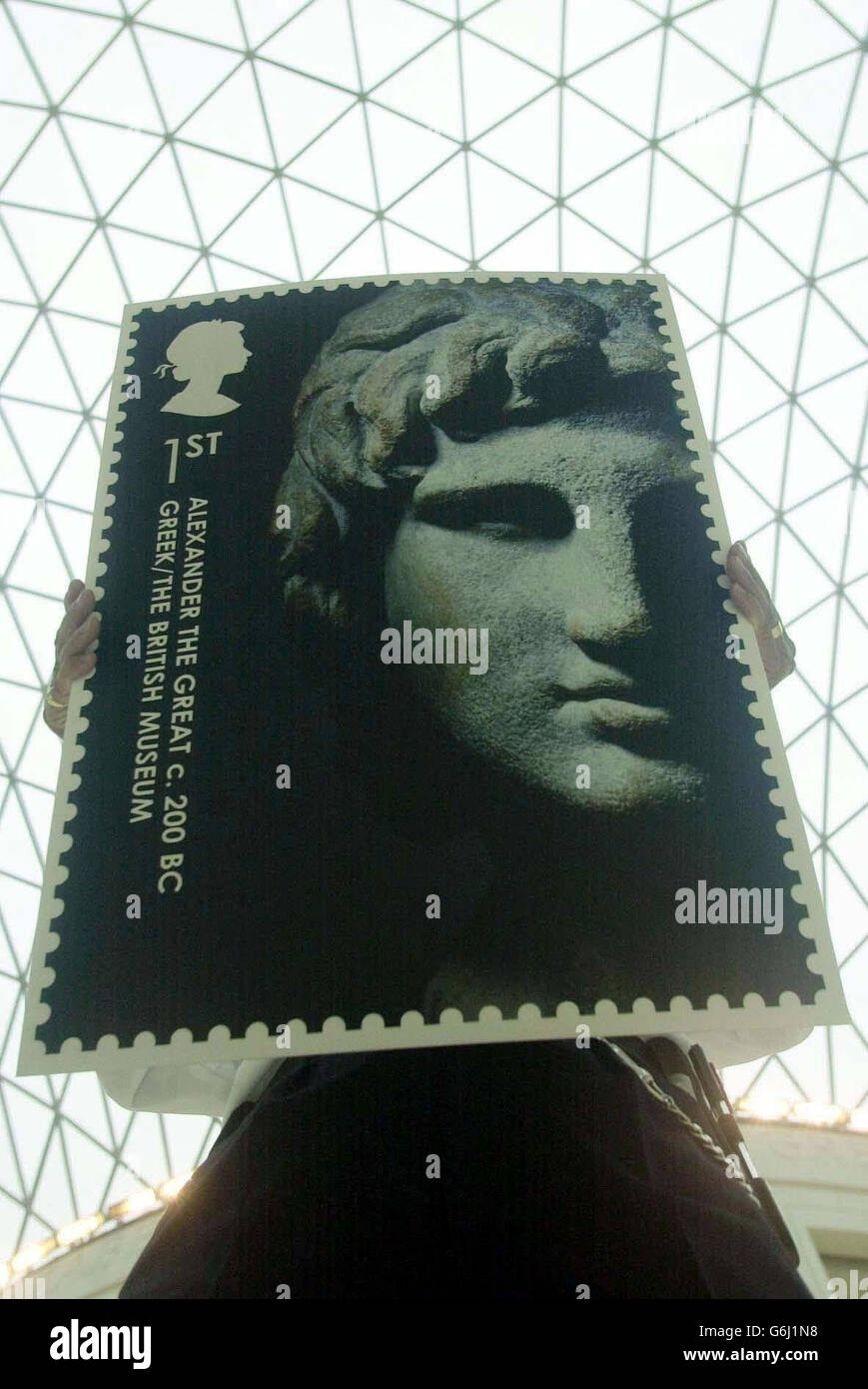 A member of staff at the British Museum in central London displaying the new first-class stamp image of Alexander The Great taken from the museum's collection of rare art and antiquities outside the museum. The Royal Mail is celebrating the 250th anniversary of the British Museum by releasing six new stamps featuring historical images, it announced. The British Museum stamp collection showcase six artefacts from five continents all from the museum itelf. The stamps will be available from 17,500 post offices from October 7. Stock Photo