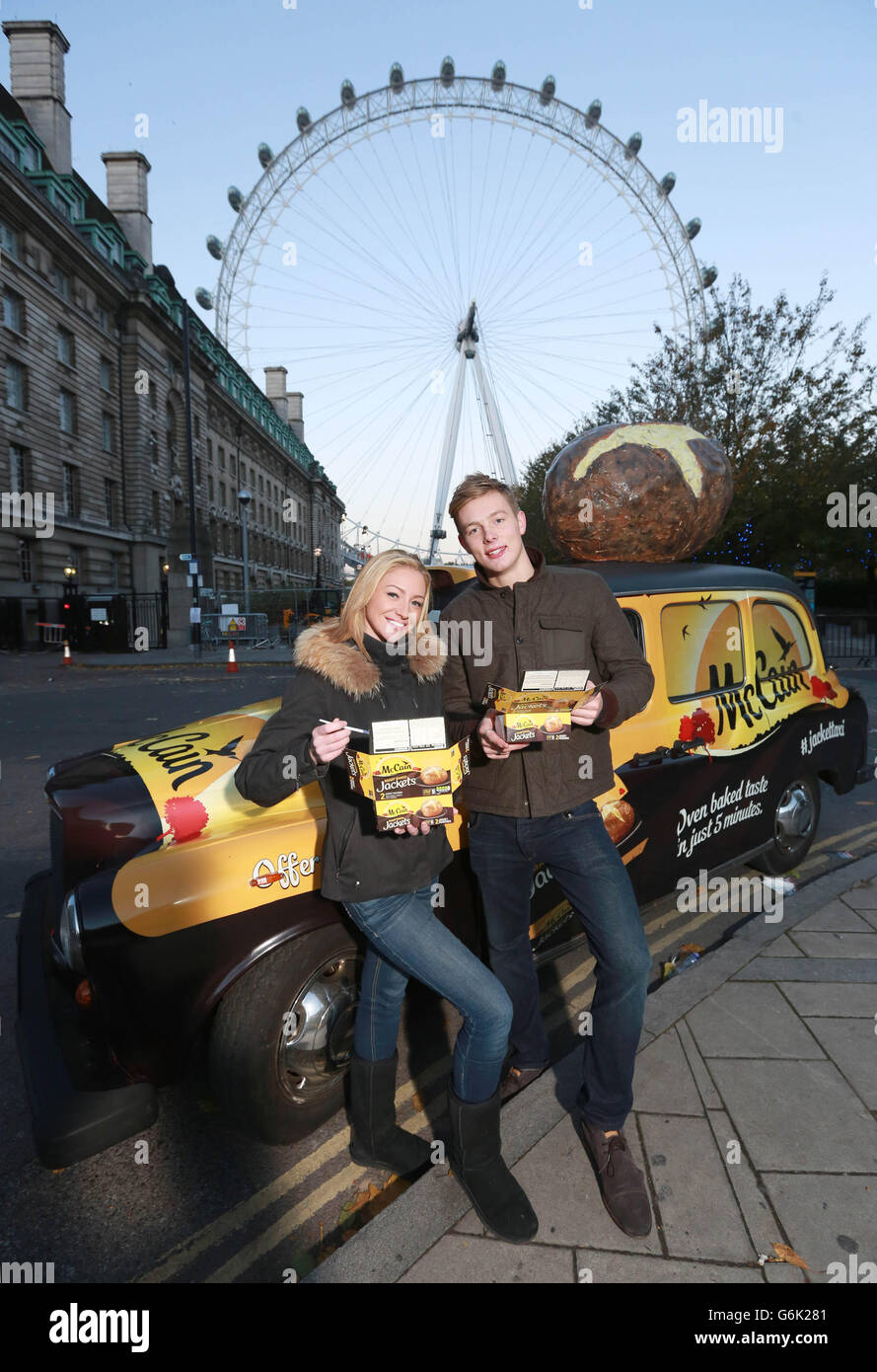 Roisin Acraman from Hertford and Hector Grenville from Finsbury Park, London, eat a McCain Ready Baked Jacket potato cooked in the Jacket Taxi, a specially modified taxi with built in potato cooking facilities, parked in front of the London Eye in London. Stock Photo