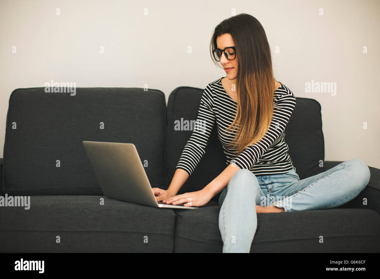 Young woman sitting on couch using laptop Stock Photo - Alamy
