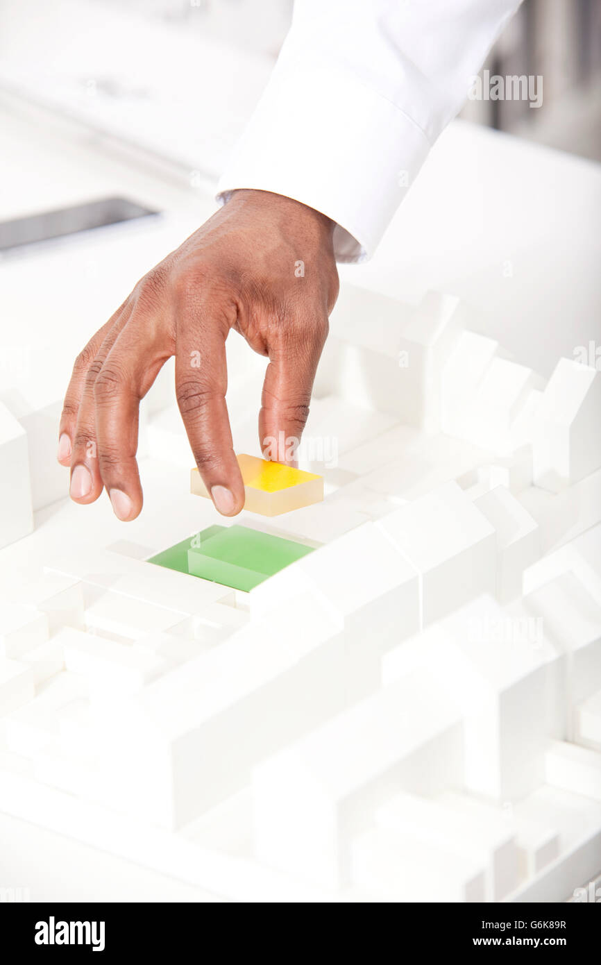 Man's hand putting building block on architectural model, close-up Stock Photo