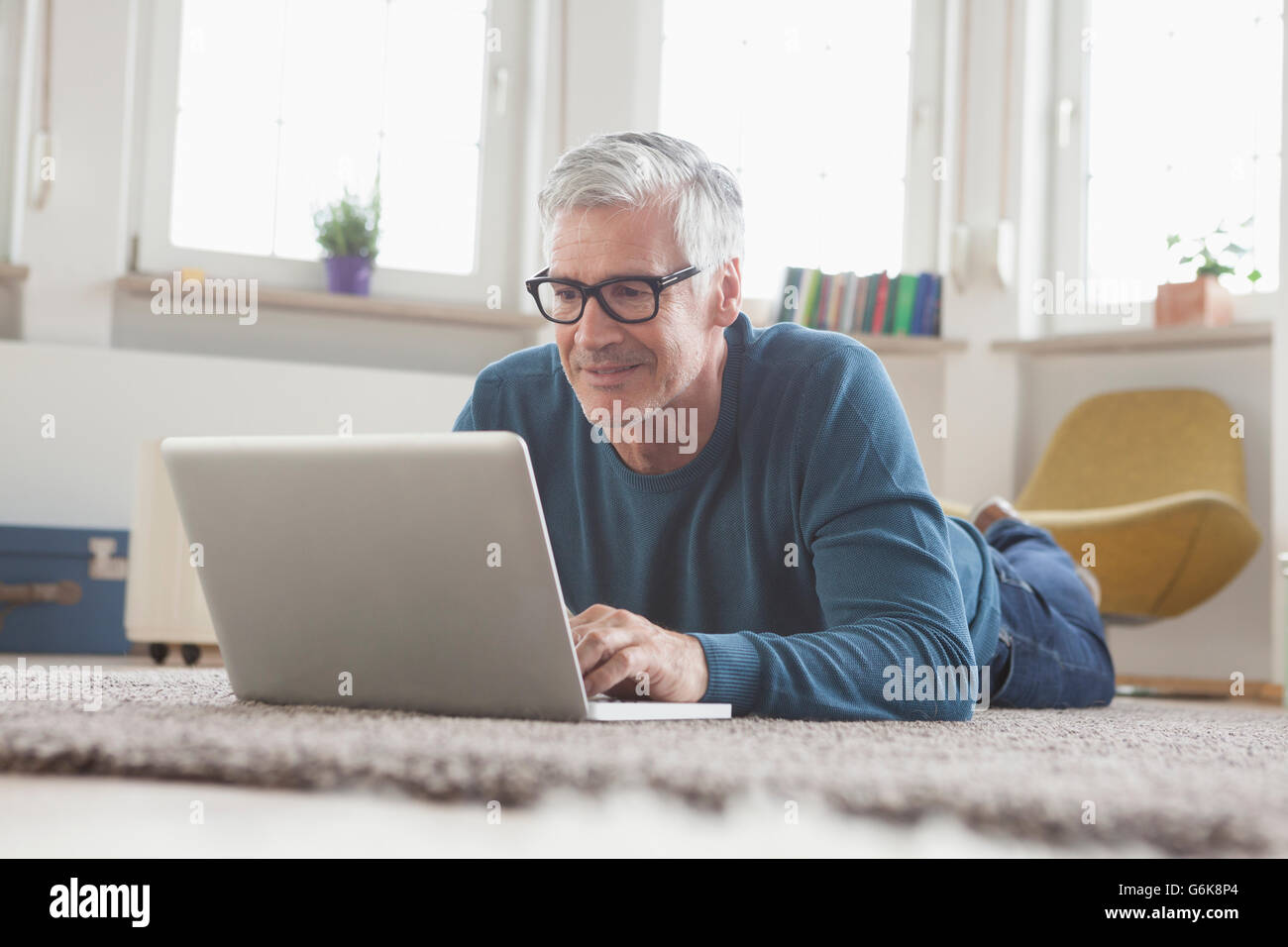 Mature man at home lying on floor using laptop Stock Photo - Alamy