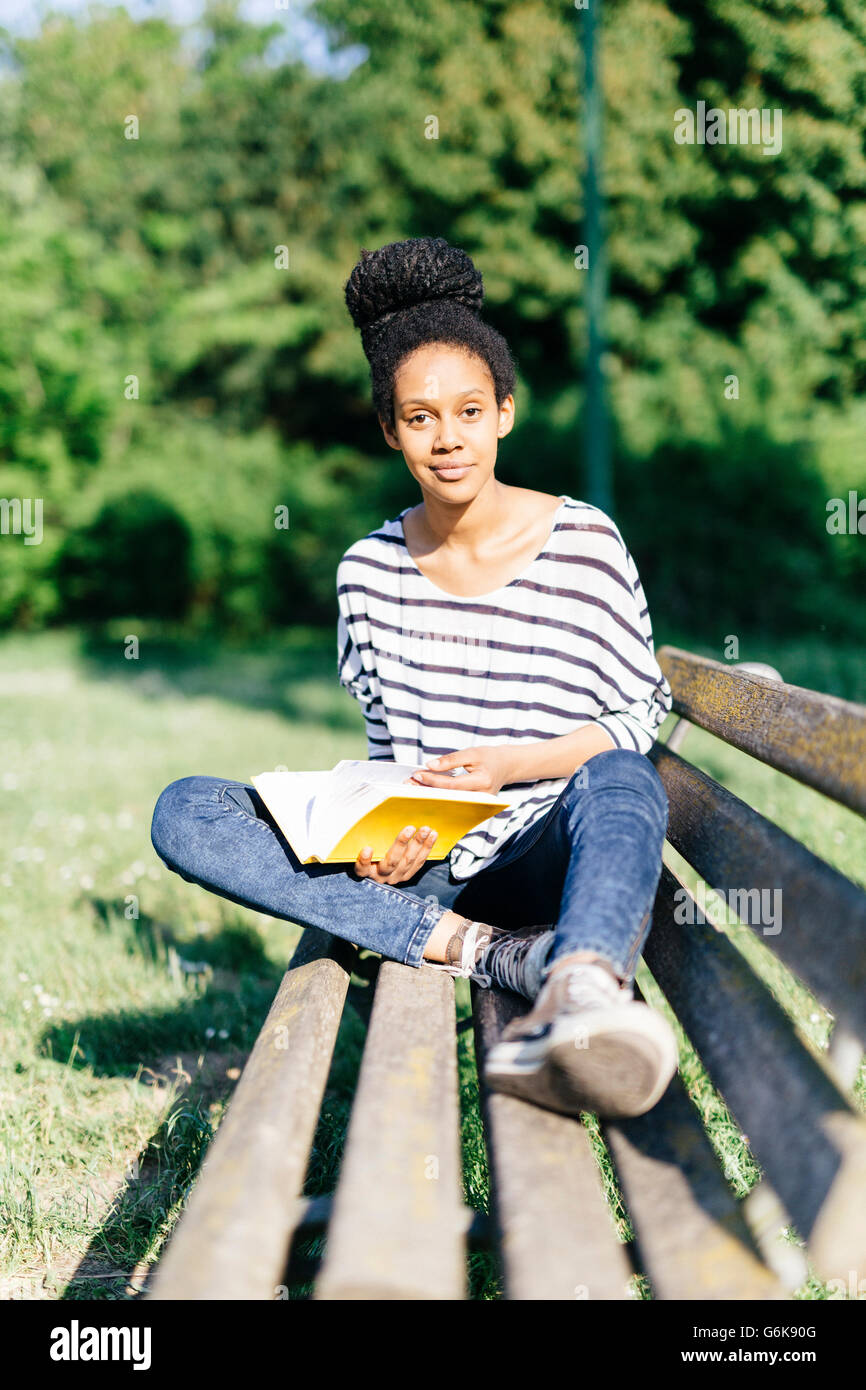 Portrait of young woman sitting on park bench with a book Stock Photo ...