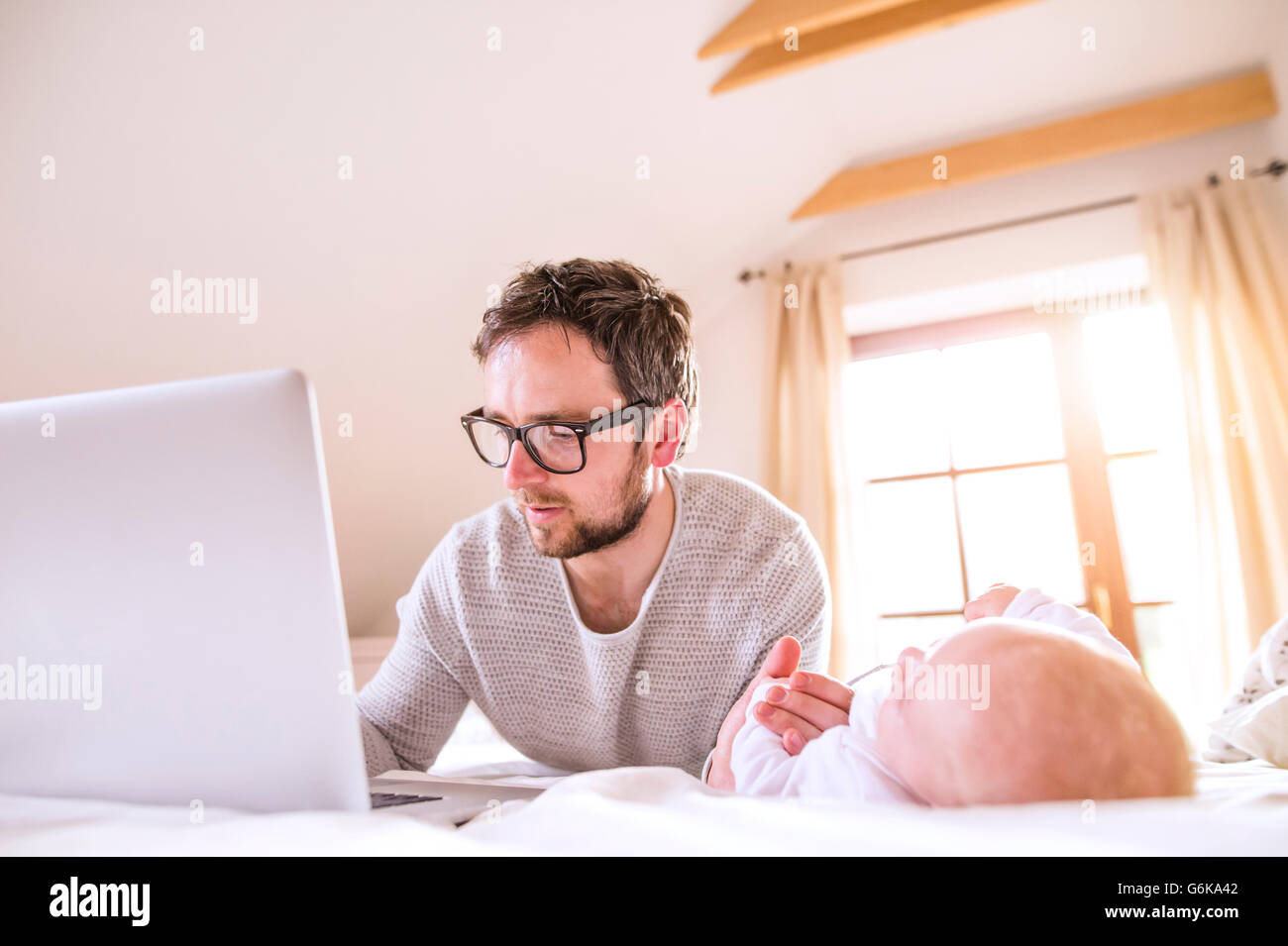 Father with baby lying on bed using laptop Stock Photo - Alamy