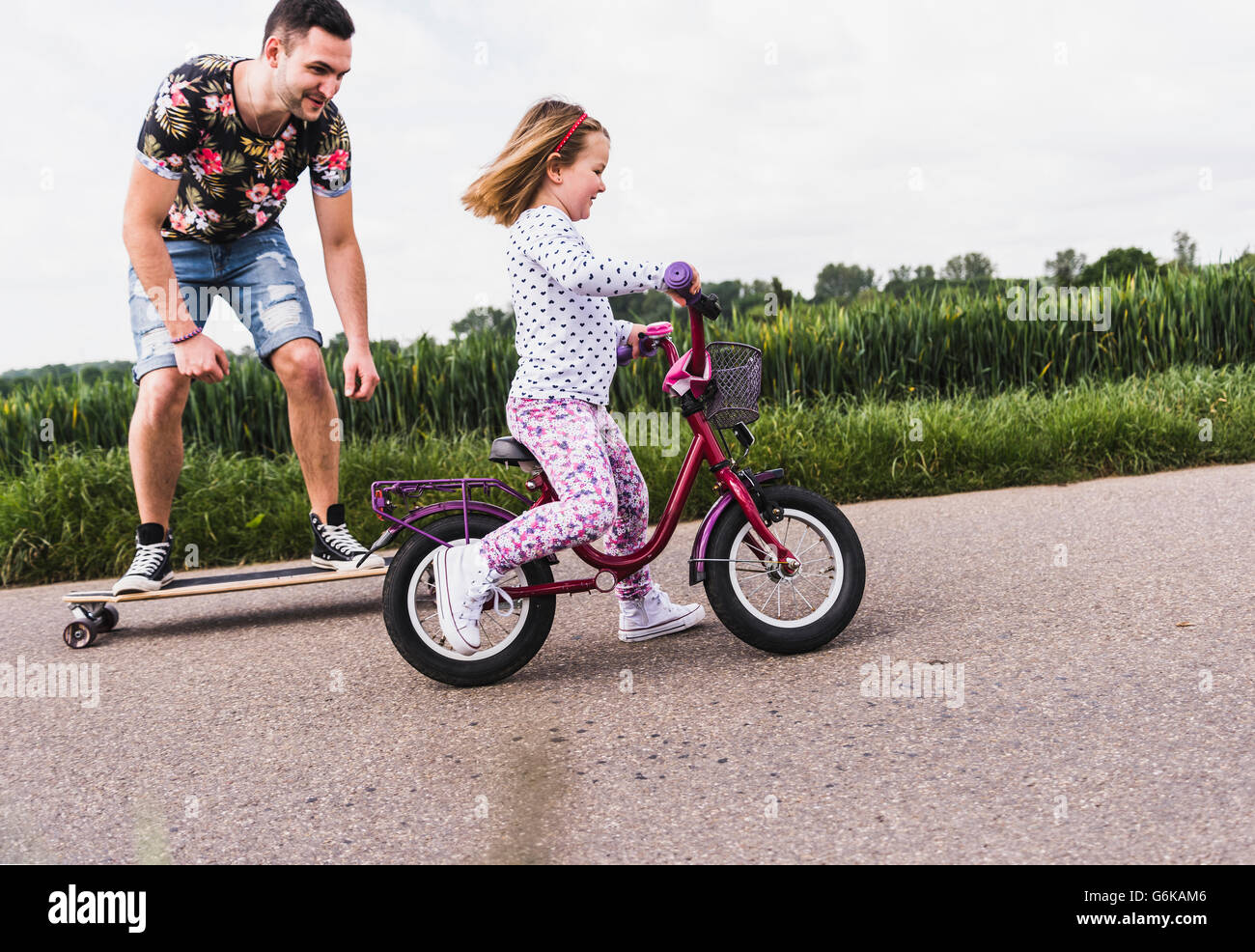 Father on skateboard accompanying daughter on bicycle Stock Photo
