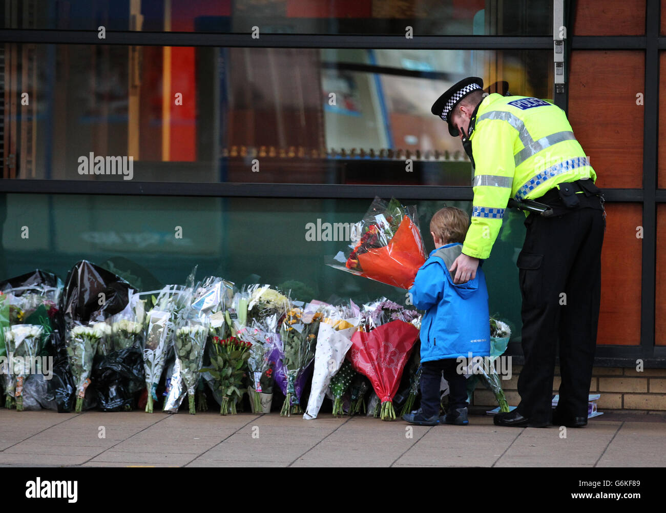 A police officer escorts a young boy as he leaves flowers near to the