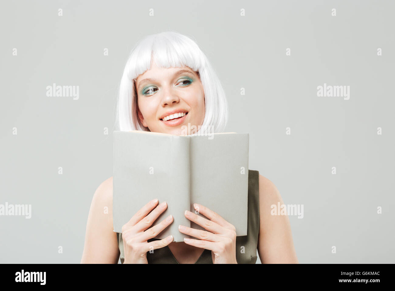 Closeup of happy lovely young woman in blonde wig smiling and reading a book over white background Stock Photo