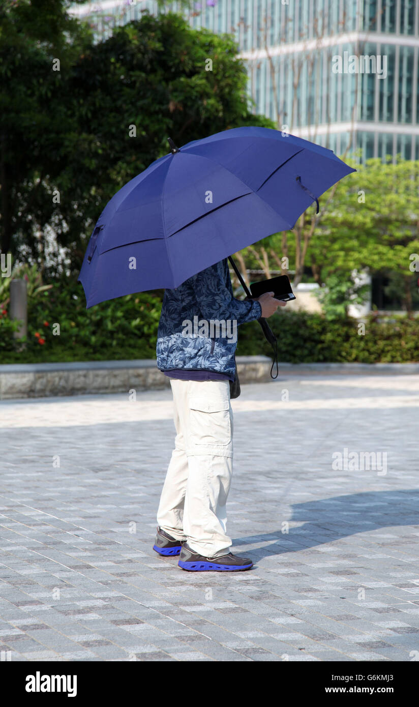 It's a photo of somebody hiding from the sun with an umbrella and using a smartphone Stock Photo