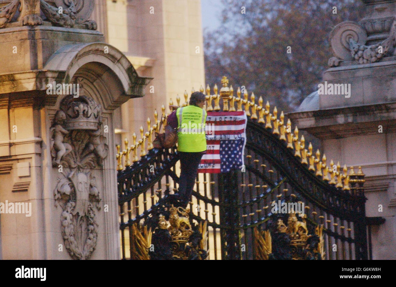 A protester stands on the gates of Buckingham Palace in London after unfurling a banner and what appeared to be a US flag carrying a slogan. Passers-by and the media were moved at least 100 metres away from the main gate during the protest by the woman who is believed to be in her 50s, and which came on the eve of US President's George Bush's arrival for his state visit to the UK. President Bush and his wife will be staying in the Palace as guests of The Queen. Stock Photo