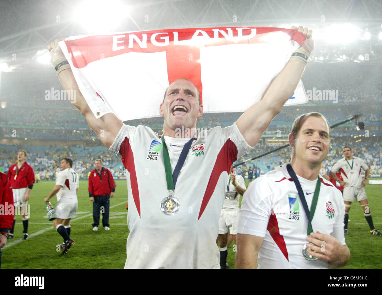 Lawrence Dallaglio holds aloft the St George's flag alongside team-mate Kyran Bracken (right) after the Rugby World Cup Final against Australia at the Telstra Stadium, Sydney, Australia. England won 20-17 after extra-time. No mobile phone use, Internet sites may only use one image every five minutes during match Stock Photo