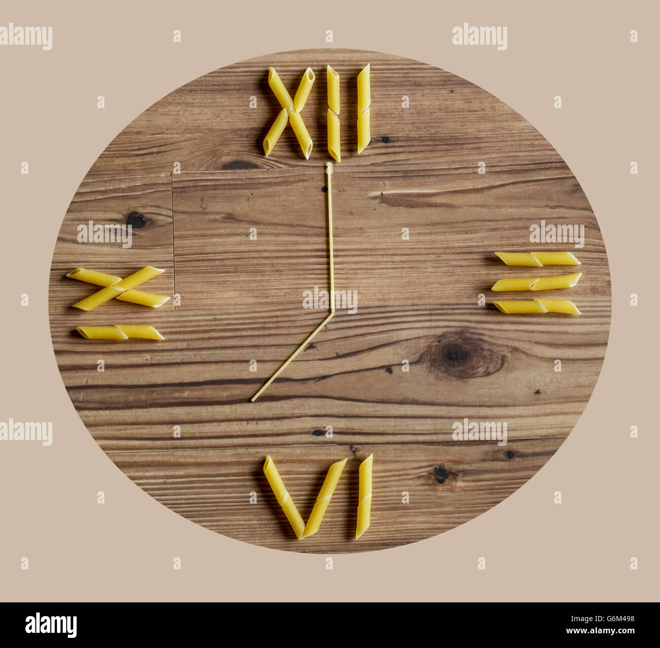 Penne pasta and spaghetti laid out on wooden background as a clock Stock Photo