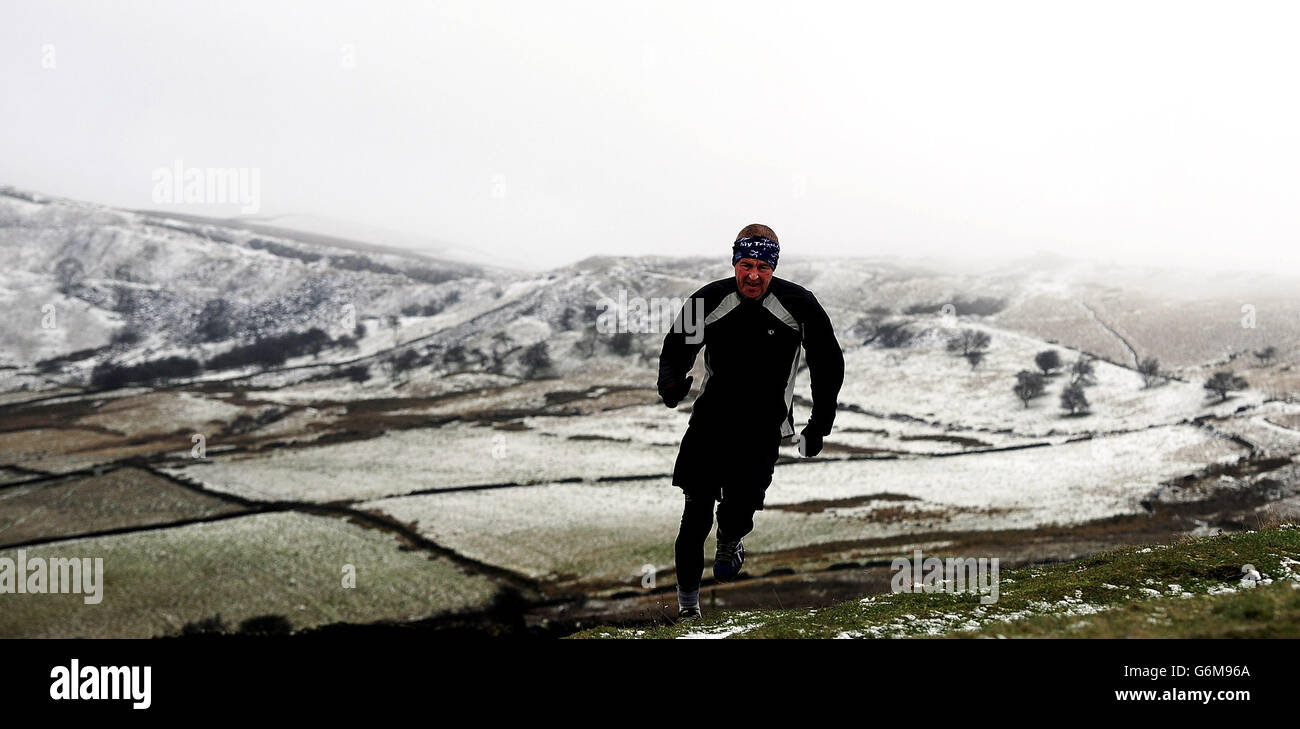 A runner braves the condition with snow on the hilltops around Buxton in the Peak District. Stock Photo