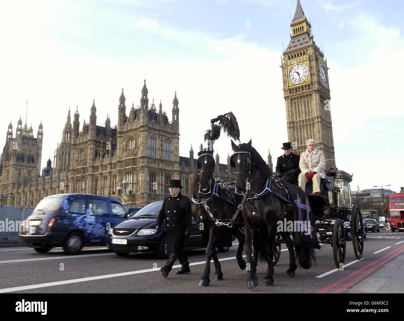 A 200-year-old horse-drawn hearse with a floral tribute to the 21,800 older people who died of the cold over the last winter, makes its way past the Houses of Parliament in Westminster, London as part of charity Help the Aged's Winter Deaths Campaign. The campaign calls for the Government to commit to adequate insulation and appropriate heating in the homes of all older people. Riding with the hearse is the television historian Adam Hart-Davis (biege coat). Stock Photo