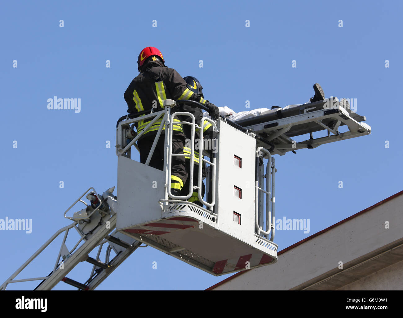brave firefighters on the fire truck cage save the wounded person with the stretcher Stock Photo