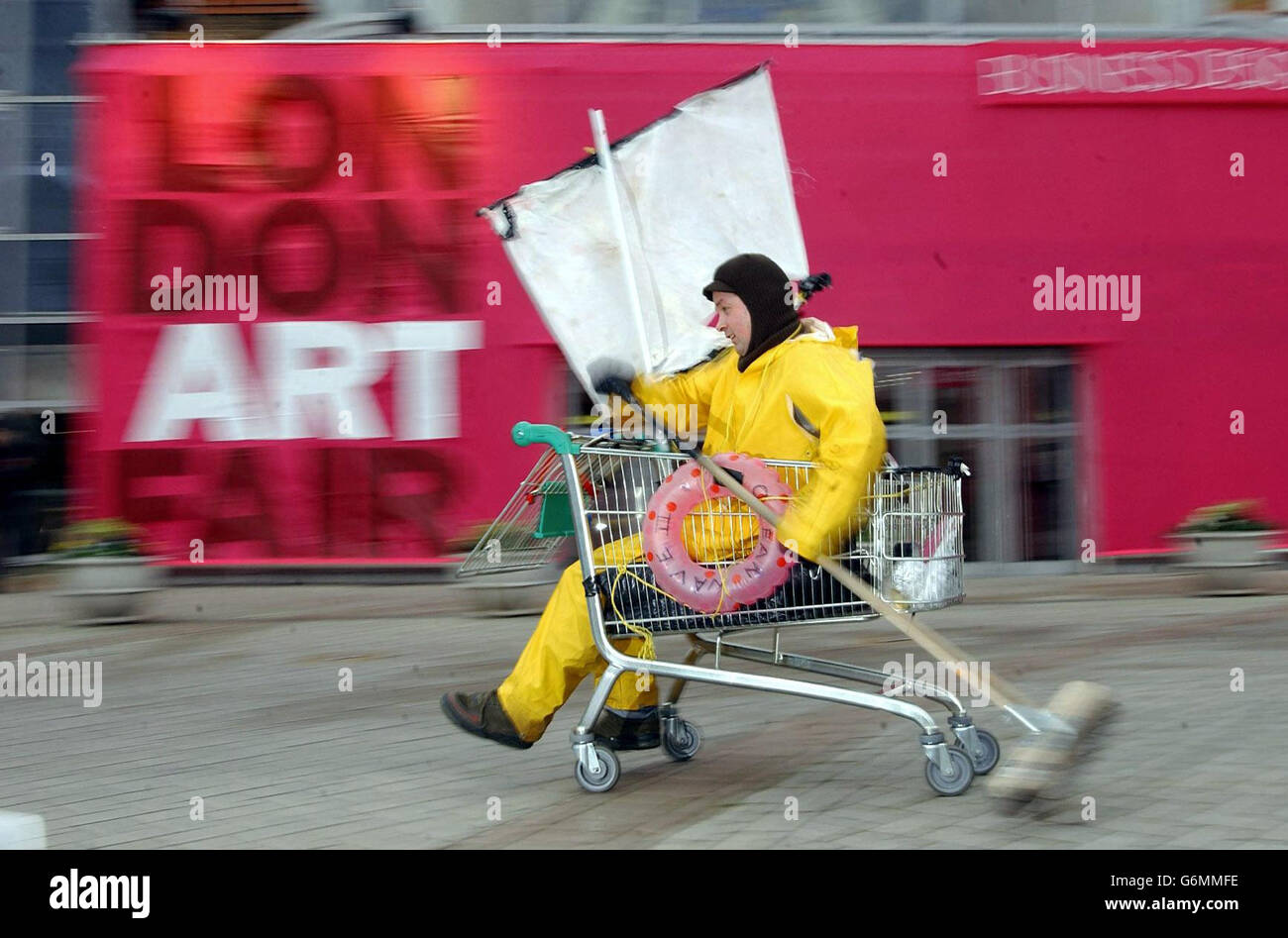 Mark McGowan, a 37-year-old artist from Peckham, south east London, propells himself along in a shopping trolley outside the London Art Fair at the Business Design Centre in Islington, North London. The performance artist is expected to start a journey to Glasgow from the Art Fair in the trolley tomorrow. The London Art Fair will run from 14-18 January 2004 and is expected to attract over 35,000 visitors. Stock Photo
