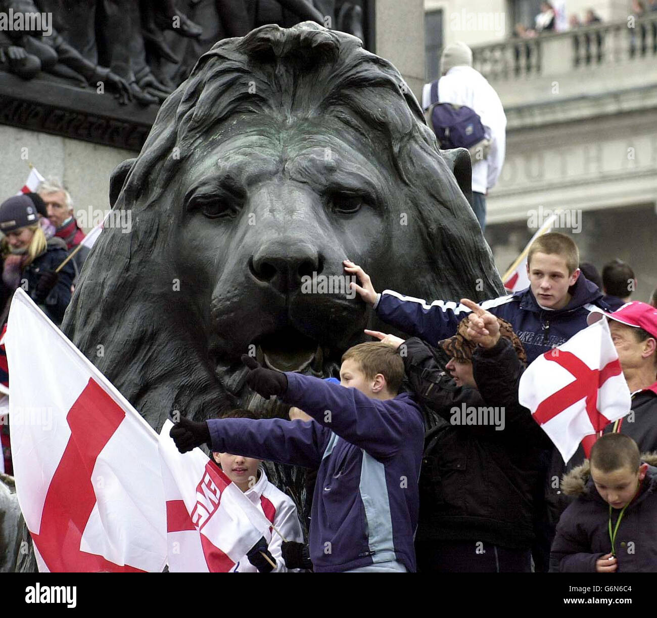 Spectators wait on a lion at Trafalgar Square to welcome Rugby World Cup players, during the Victory Parade in London. Later the England Rugby World Cup winners were travelling to receptions at Buckingham Palace and Downing Street. Stock Photo