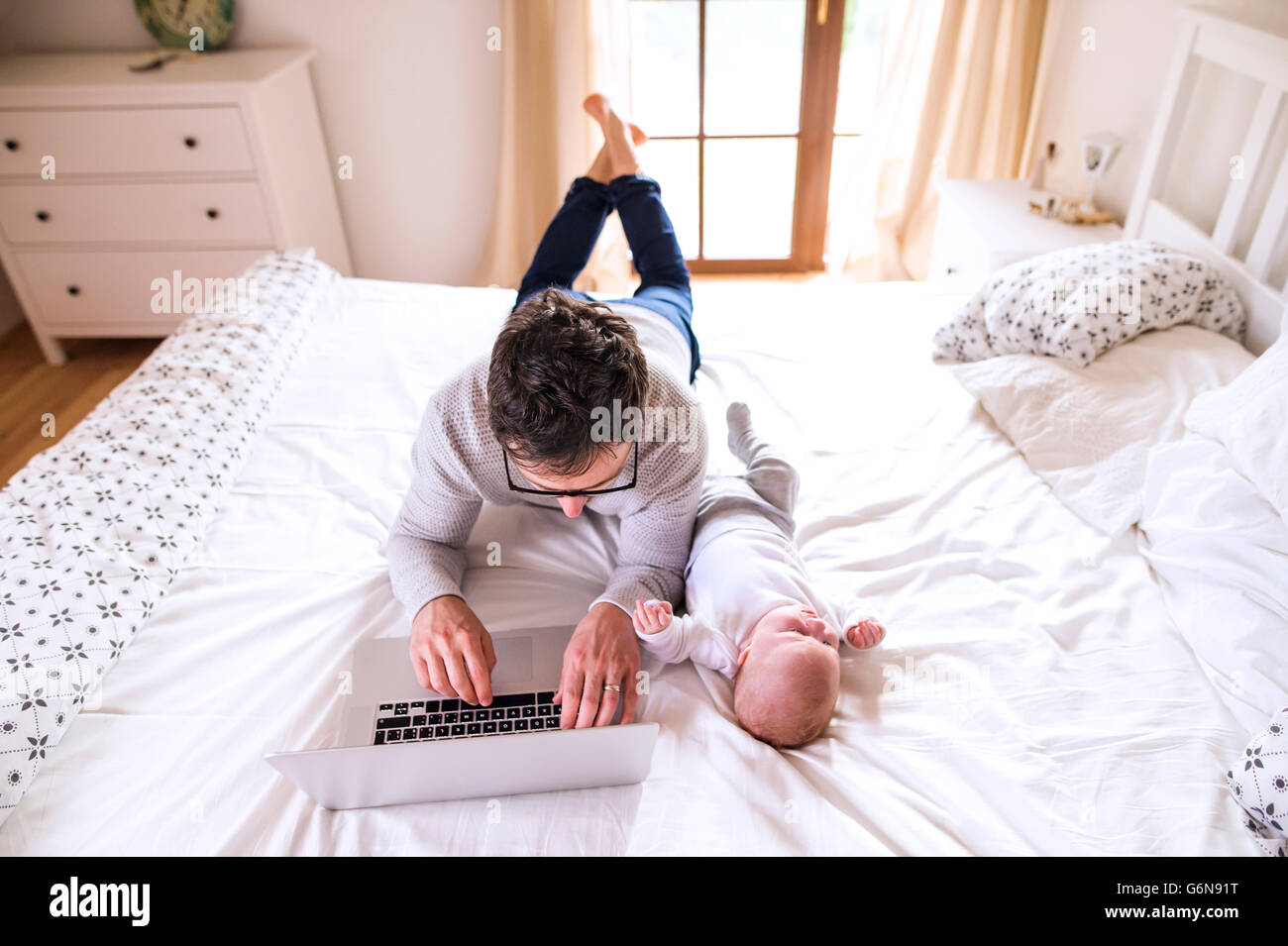 Father with baby lying on bed using laptop Stock Photo - Alamy