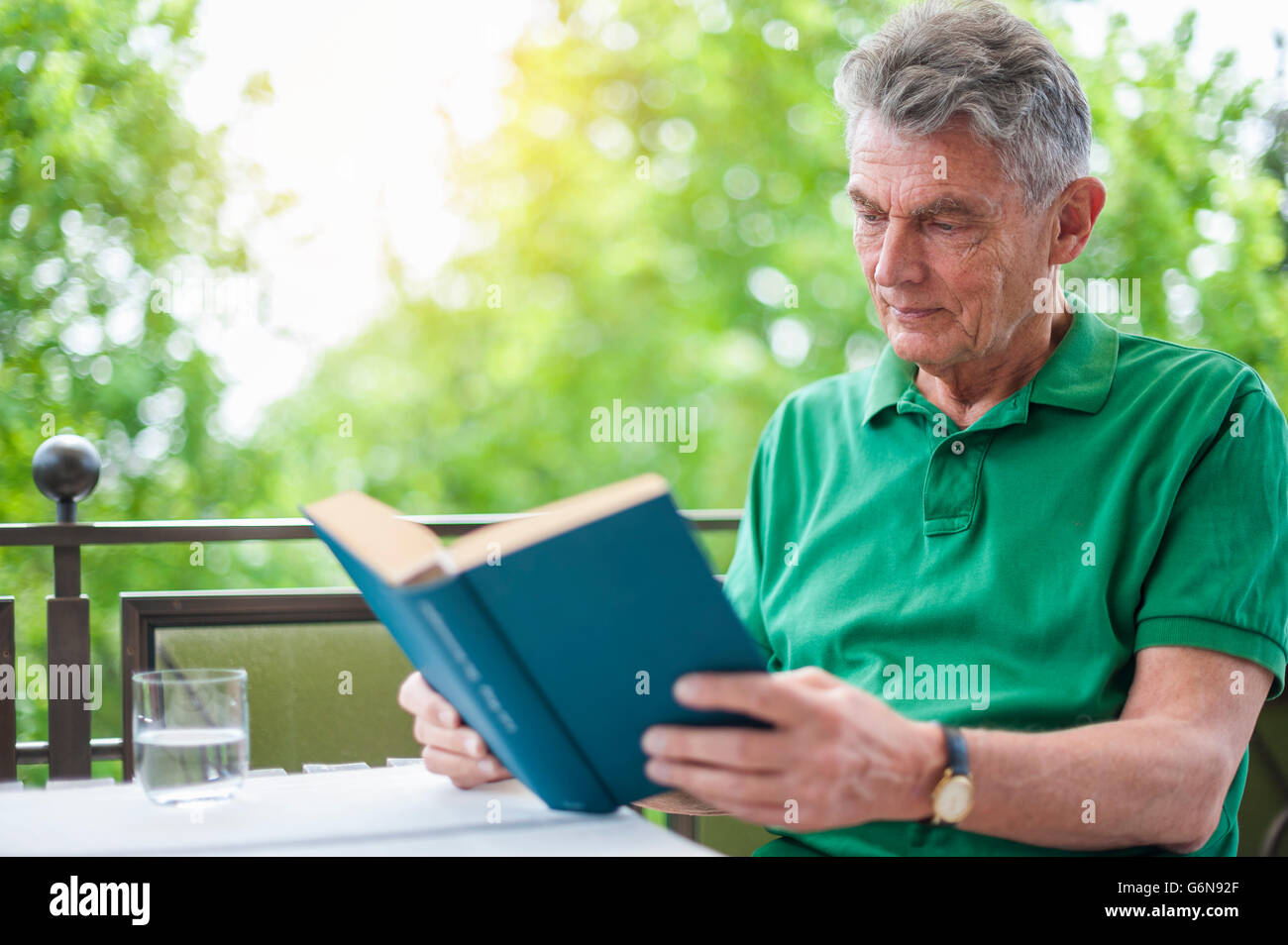 Senior man sitting on balcony reading a book Stock Photo