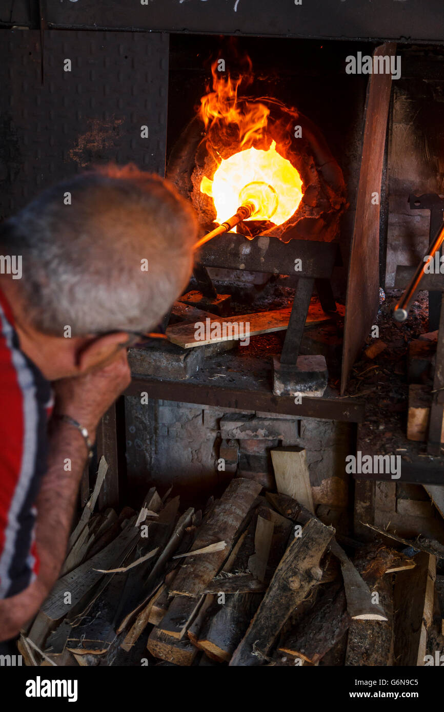 Man blowing glass with a tube using a furnace in a glass factory in