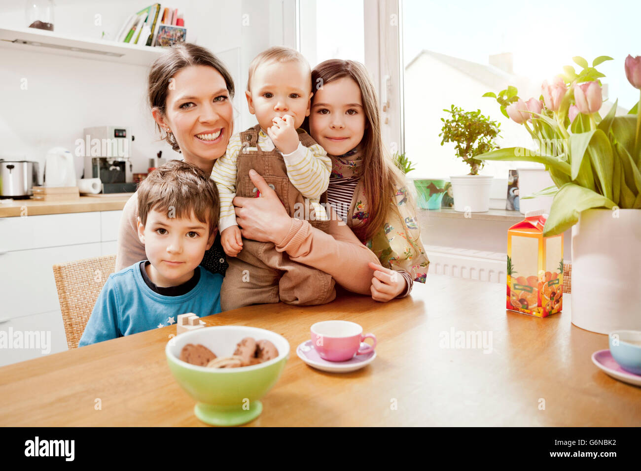 Portrait of happy mother with her three little children in the kitchen Stock Photo